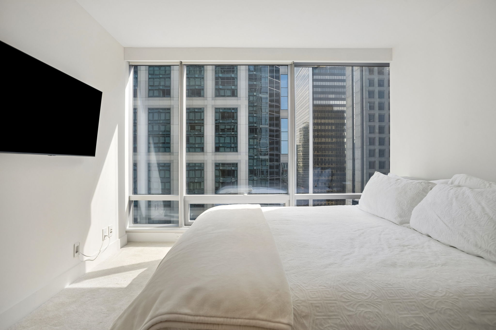 The bedroom, with a wall-mounted television and windows onto the neighbouring towers.