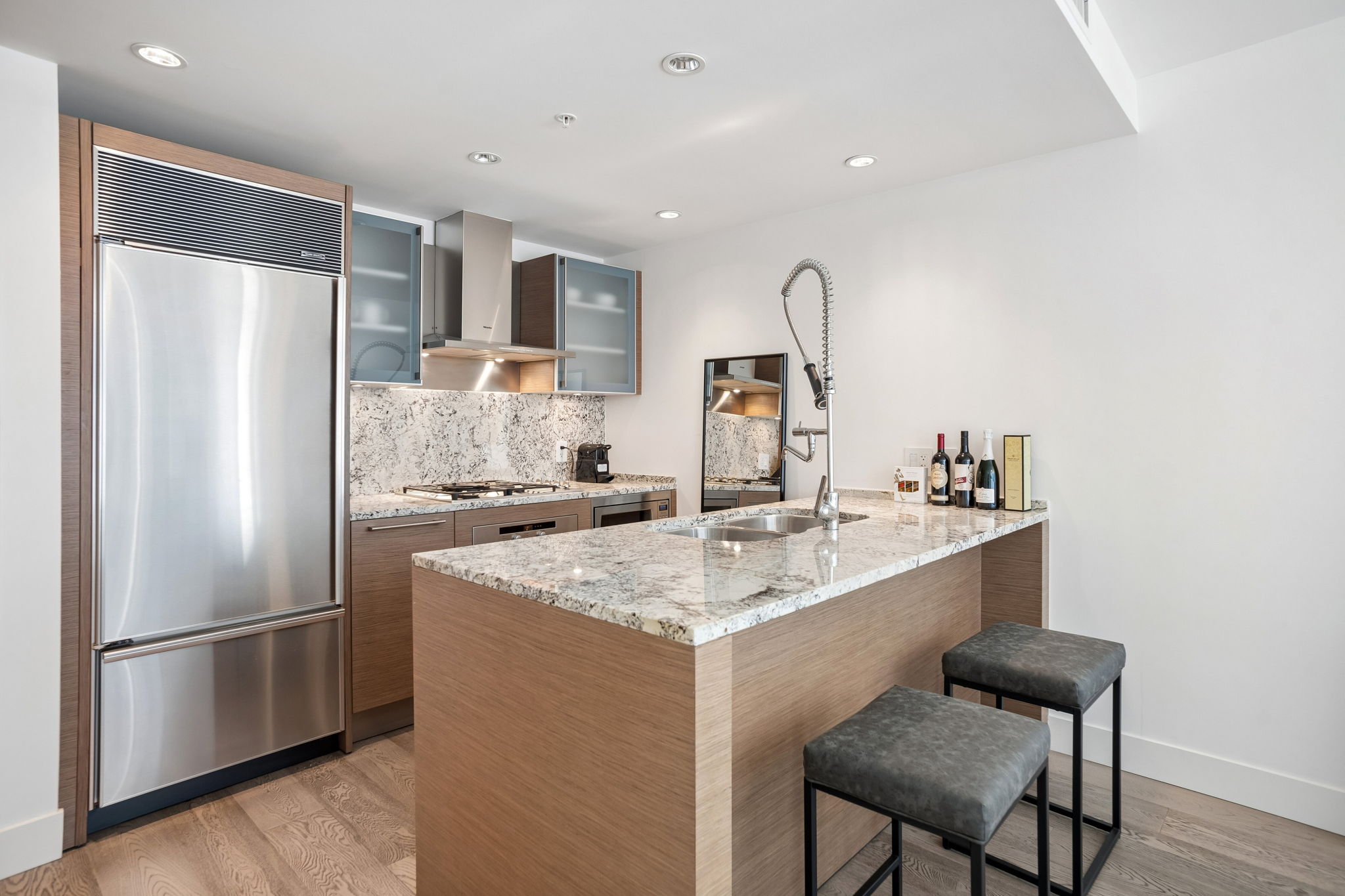 The kitchen island in oak with a granite counter, integrated refrigerator and two bar stools.