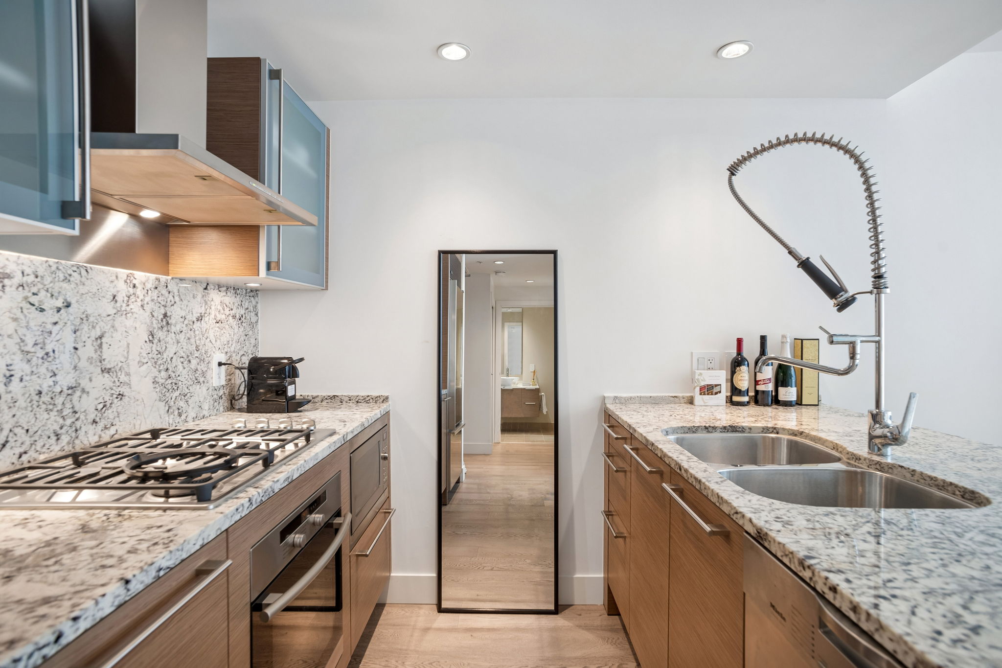 The kitchen along its length, with a gas cooktop, wall oven and a double sink under the cabinets.