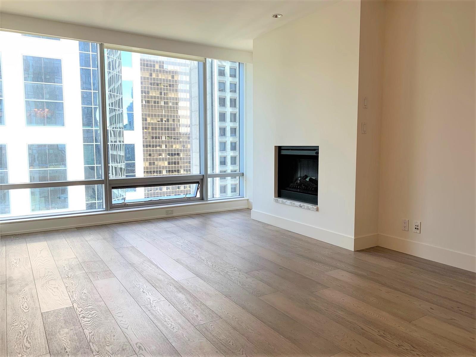 The living room, hardwood running to a window wall on the left and the fireplace set into the far wall.