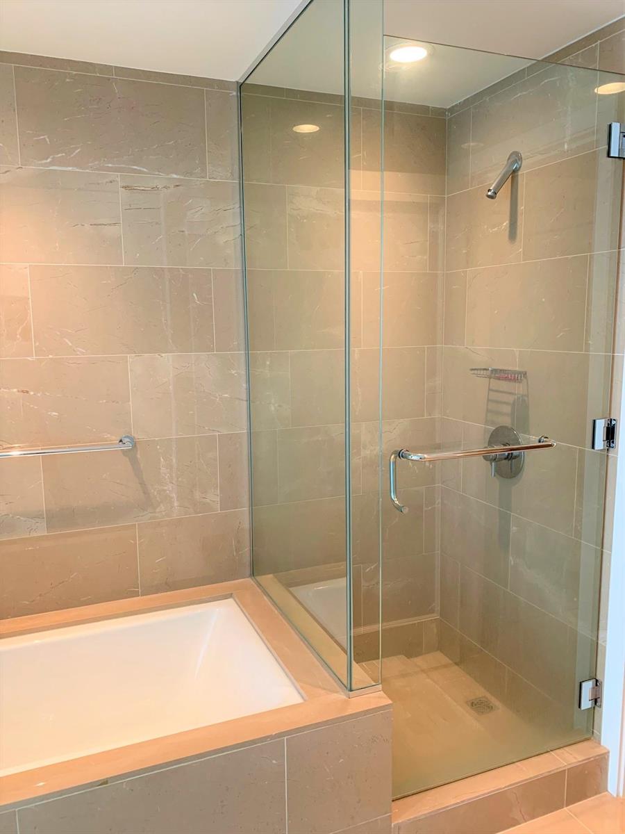 The bathroom, a glass shower beside the tub with stone tile to the ceiling.