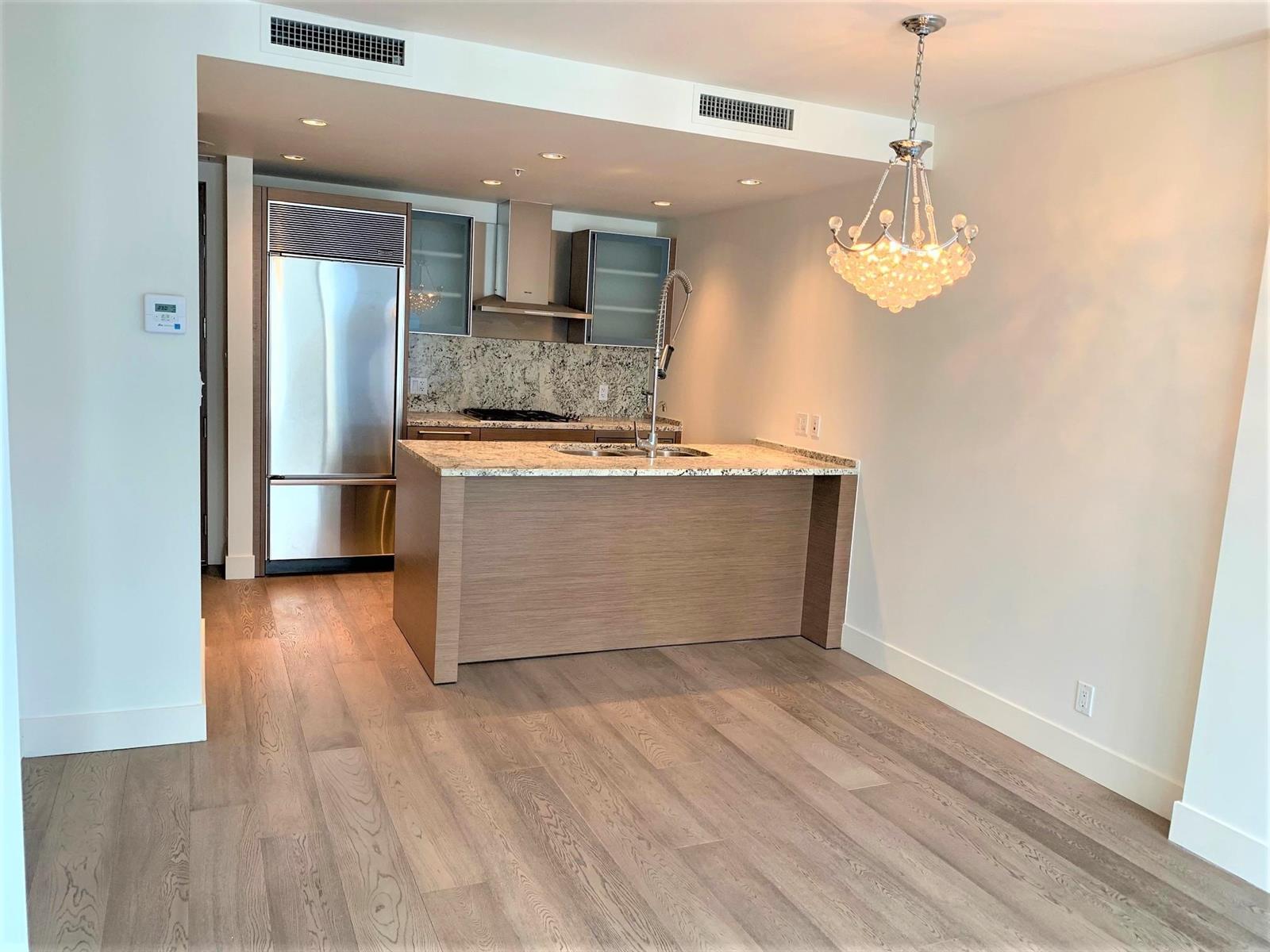 The kitchen from the living room, a long island under a chandelier with the entry hall beyond.