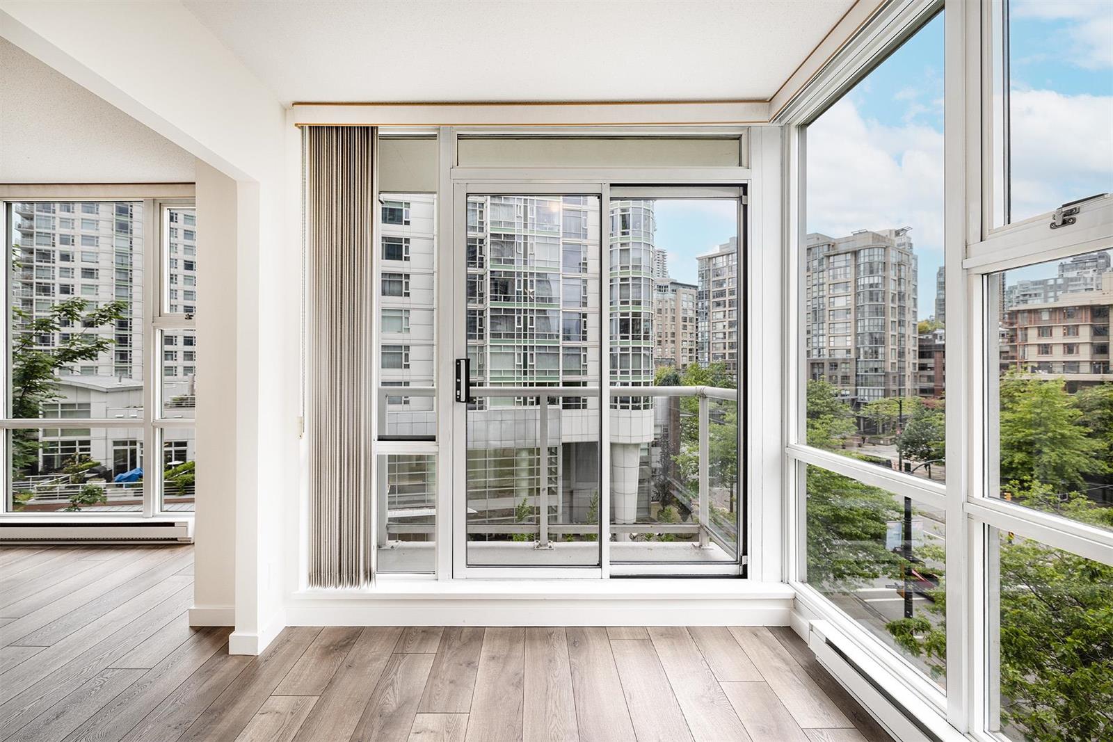 The living room corner, where the glass turns: a sliding door to the balcony between two walls of window, with towers and trees beyond.