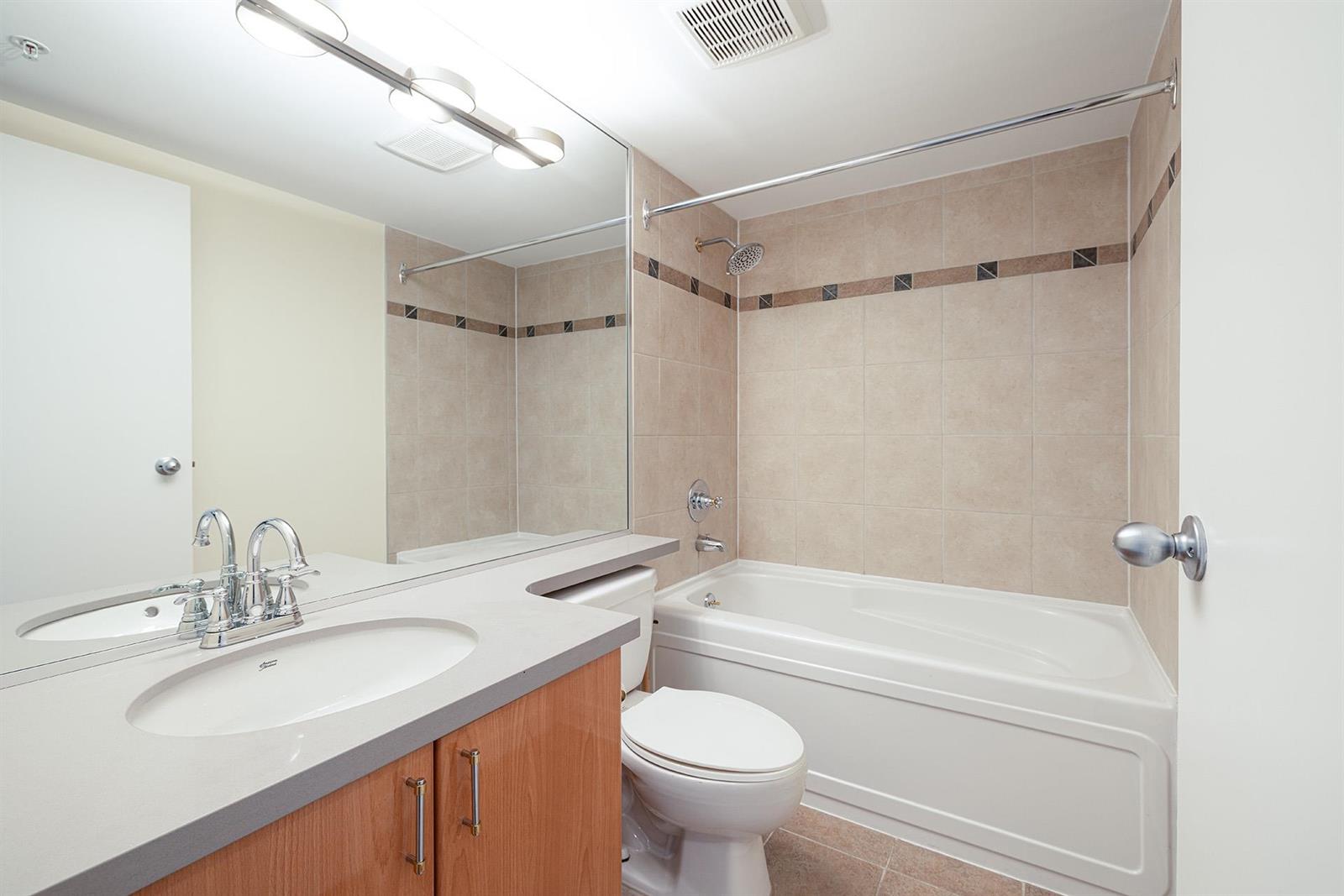 The bathroom, with a wide mirror over the vanity and a tiled band running around the tub and shower.