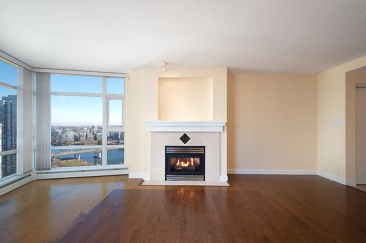 The living room, a lit gas fireplace in a tiled surround with the corner windows beside it looking down False Creek to the Cambie Bridge.