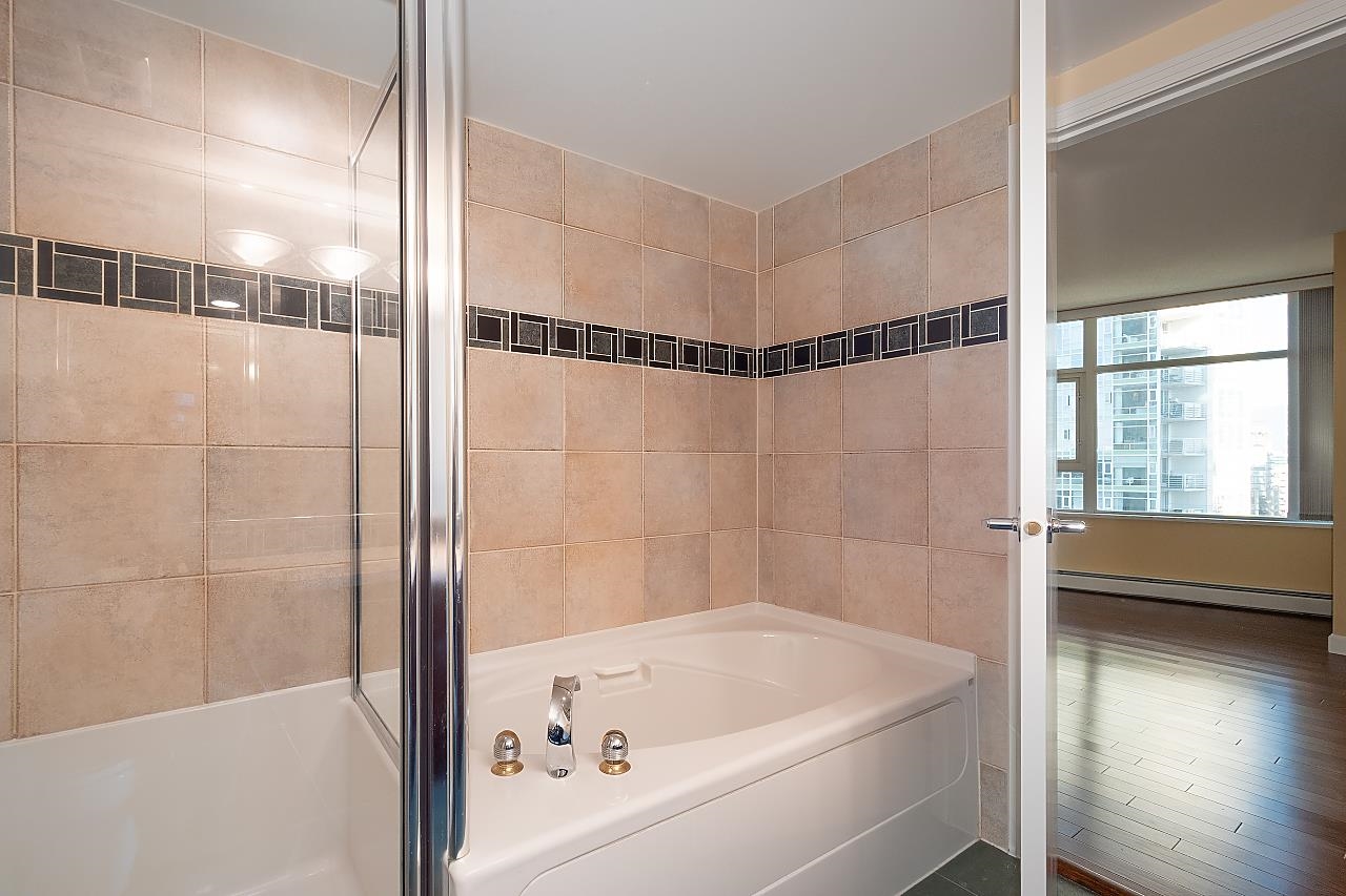 A bathroom, a soaker tub tiled to the wall behind a glass screen, with a bedroom through the open door.
