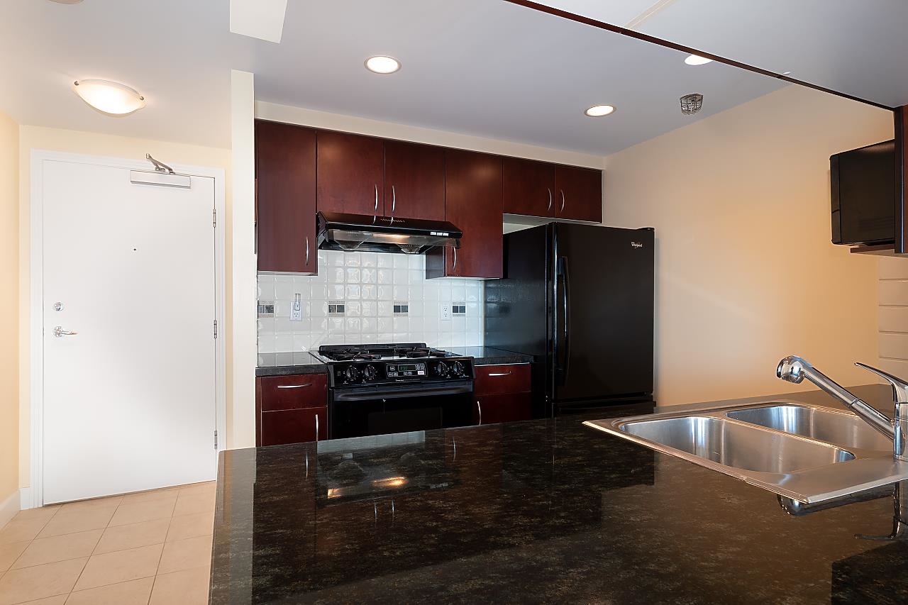 The kitchen, a gas range under a hood with a tiled splashback and the fridge beside it.