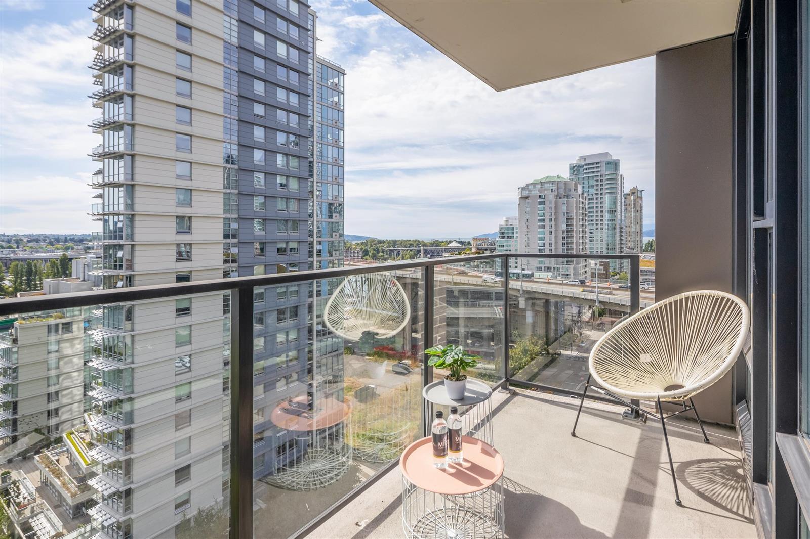 The balcony, two round chairs with the neighbouring towers beyond the glass rail.