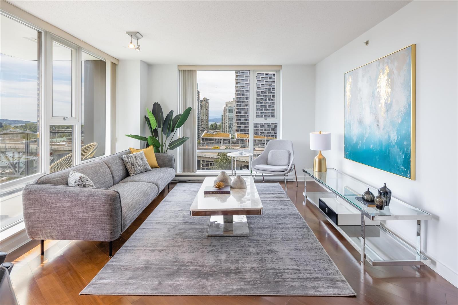 The living room, a grey sofa and a glass coffee table on a pale rug, with a painting of water on the far wall.