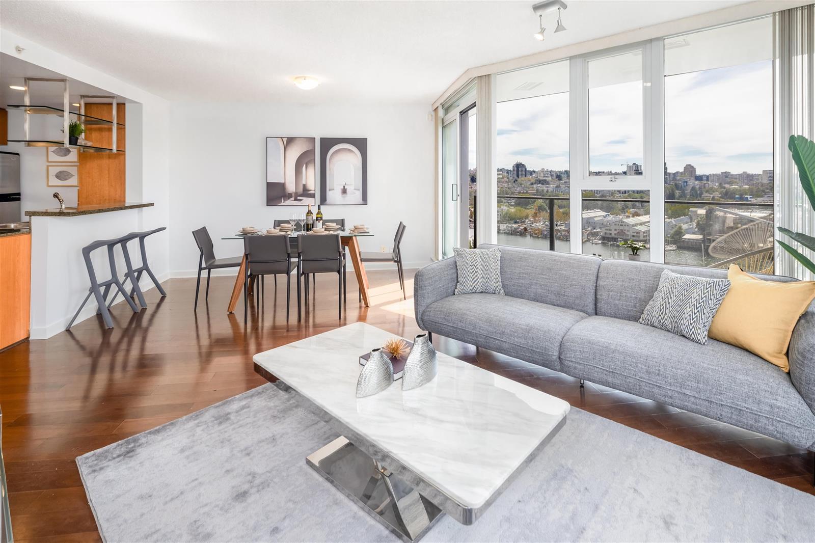 The living room from the window end, a marble table between the sofas and the kitchen open behind.