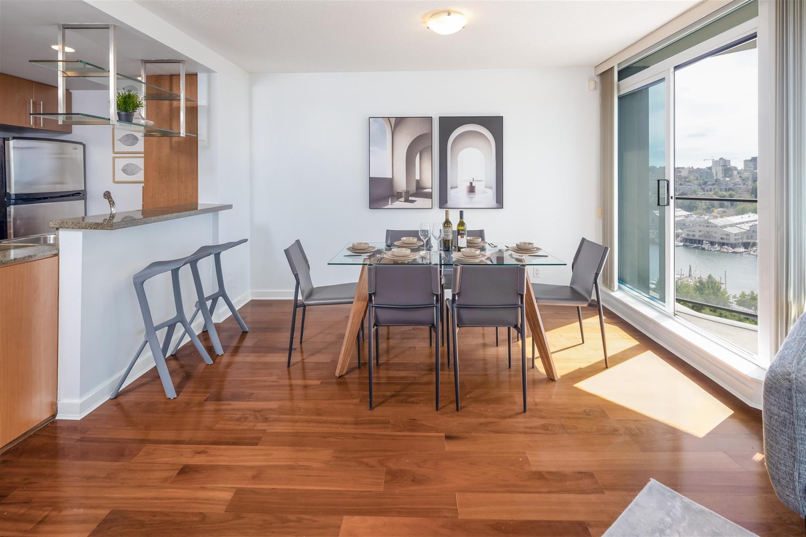 The dining table under the windows, six chairs around it and the kitchen bar along the left.