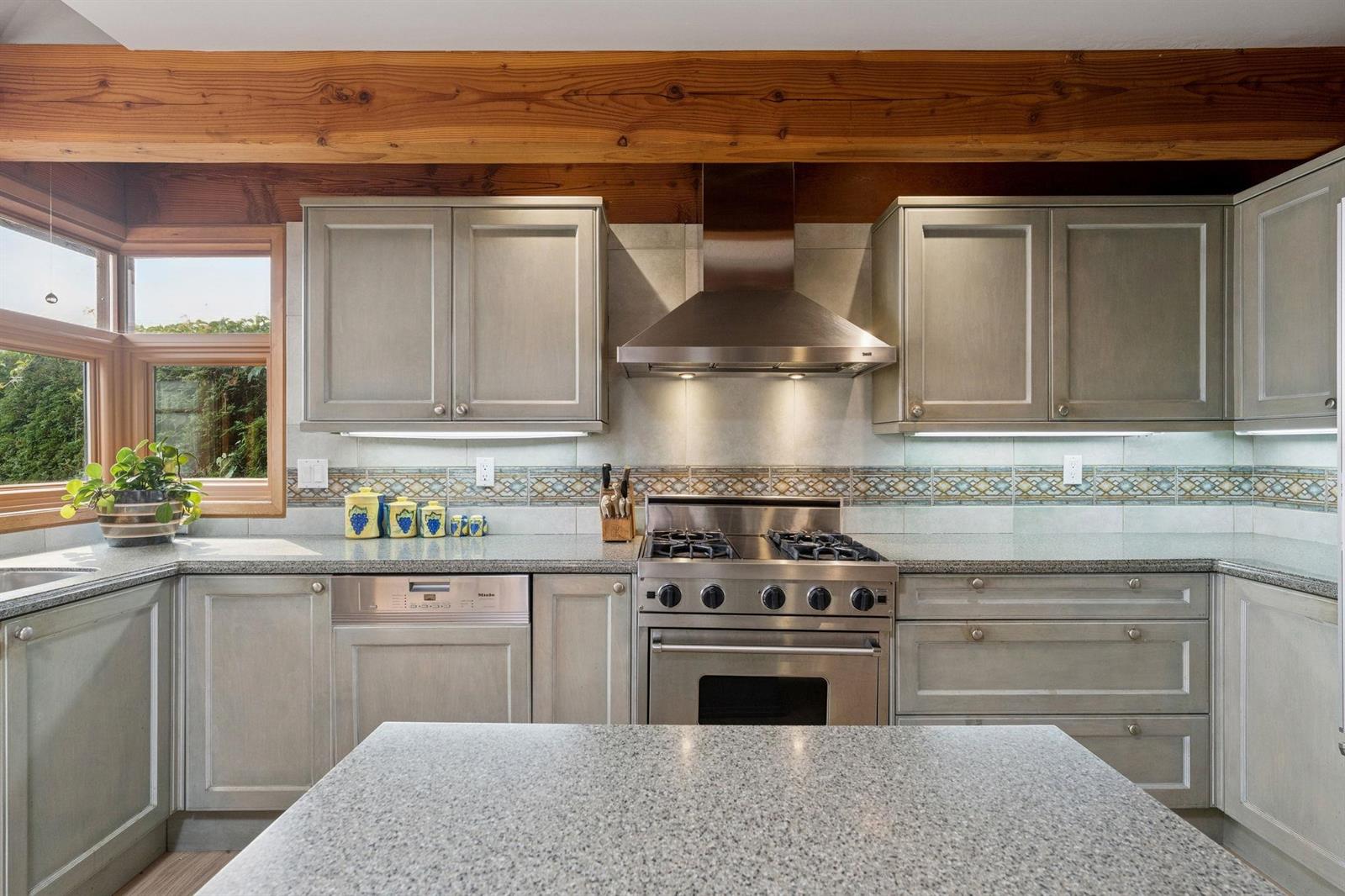 The kitchen work wall, gas range and hood between stone counters and glass cabinets.
