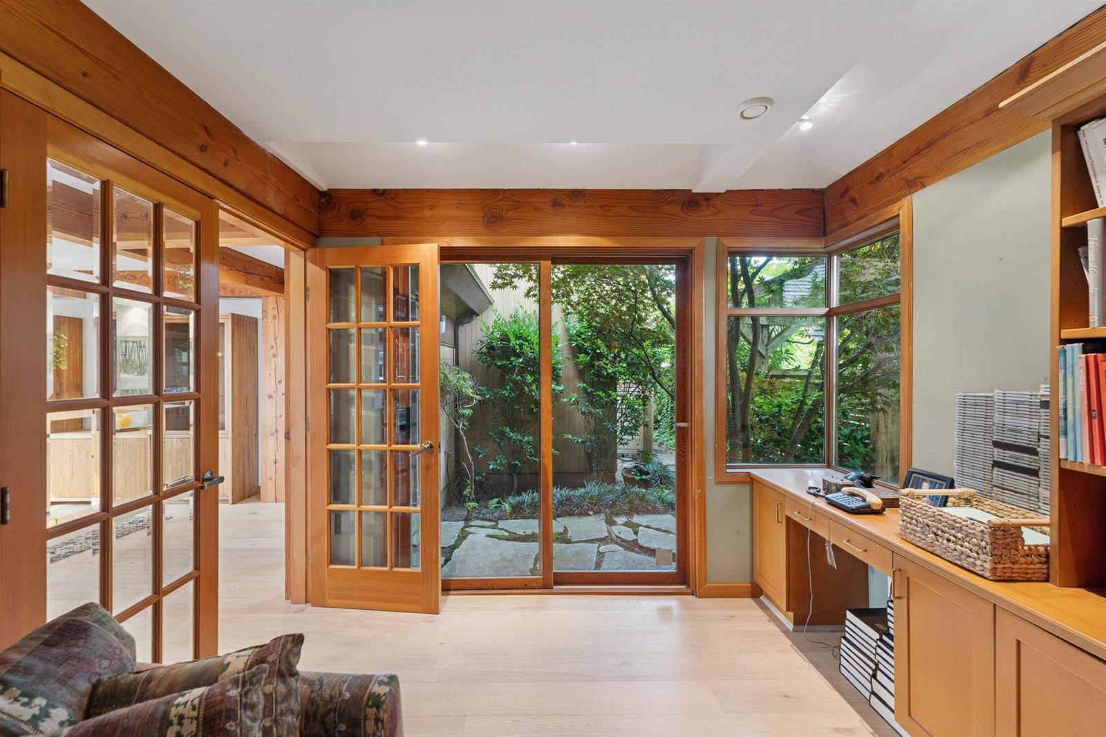 The den, a desk and cabinets under a beamed ceiling with french doors to the patio.