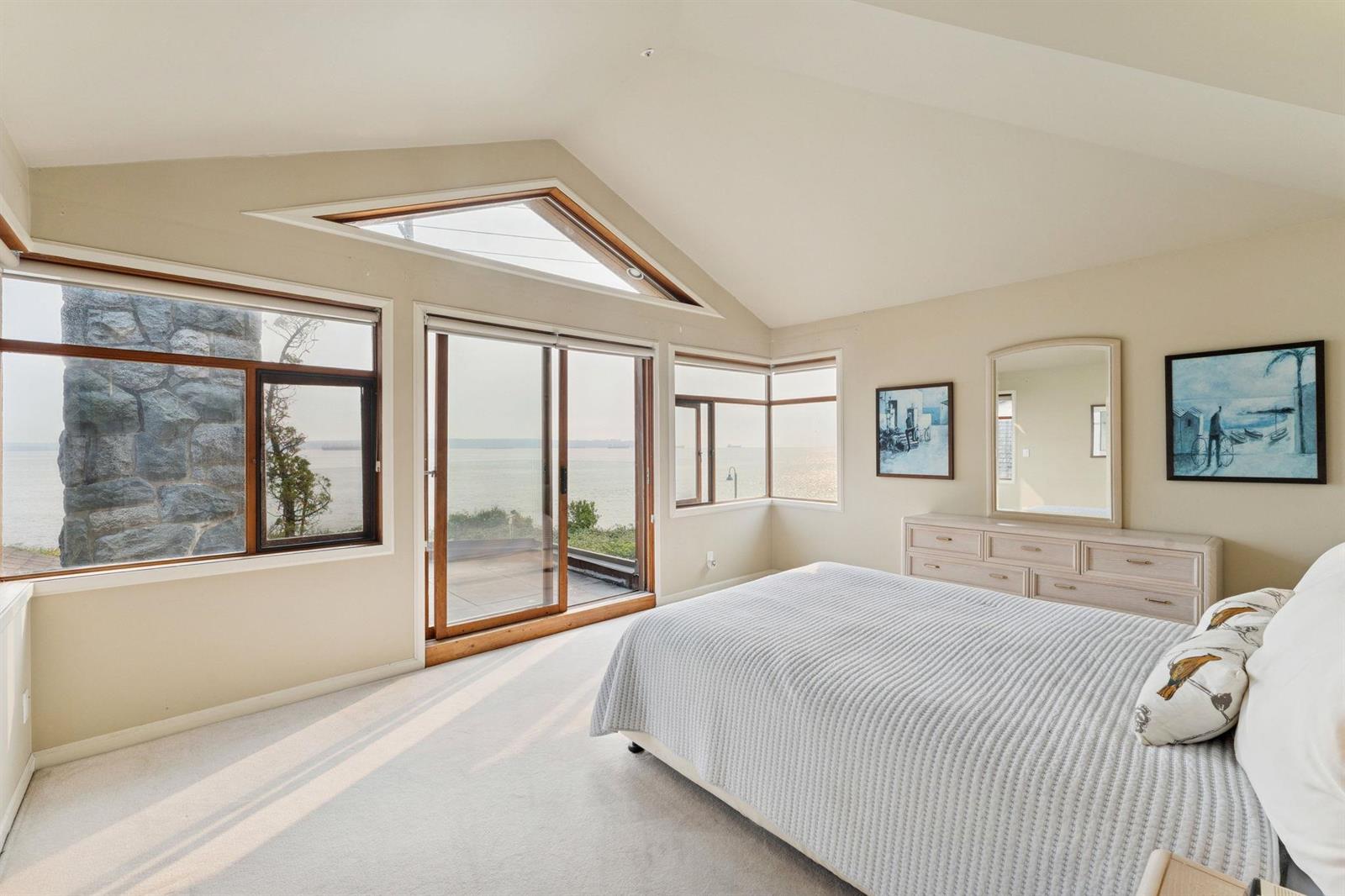 The primary bedroom, the bed against a pale wall with windows on two sides.
