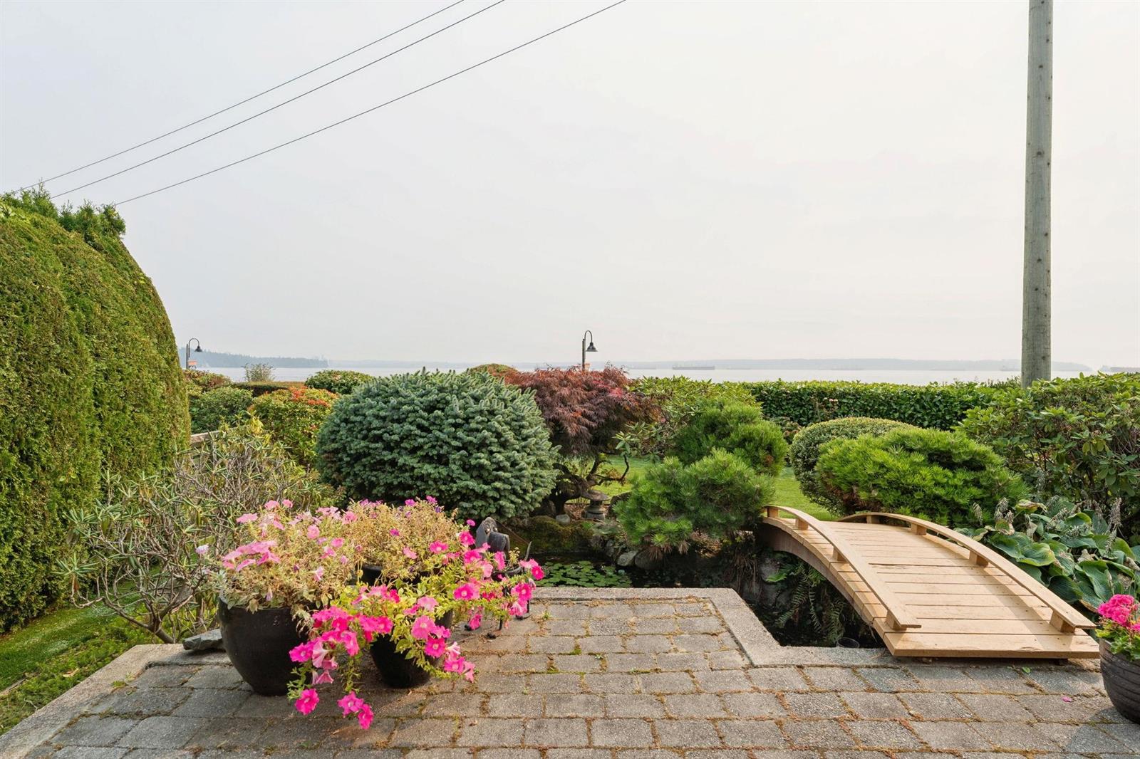 The garden from the patio, flowers and clipped shrubs along a stone path.