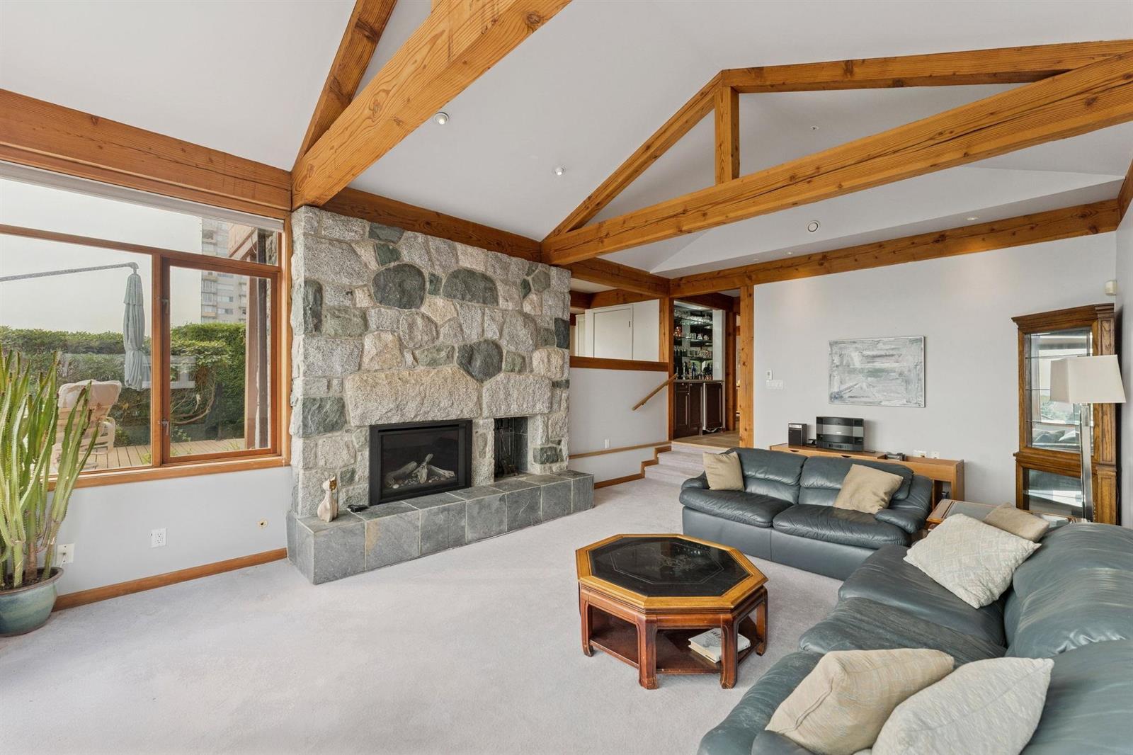 The living room from the other end, vaulted timber beams overhead and a seating group by the fire.