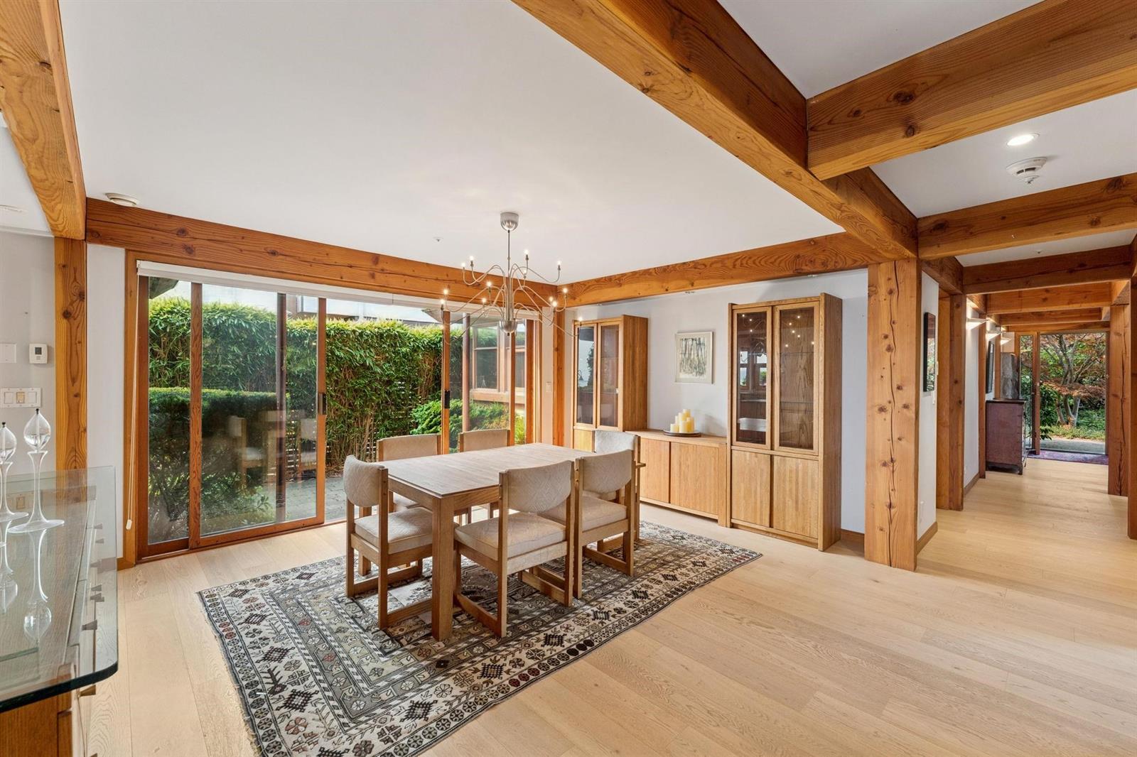 The dining room from the hall, timber beams overhead and the garden beyond the glass.