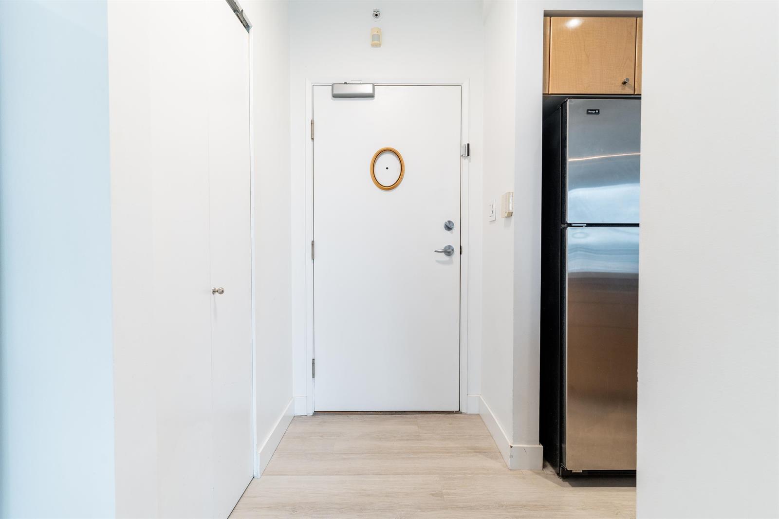 The corridor at the suite door, looking in past it to the refrigerator and the kitchen.