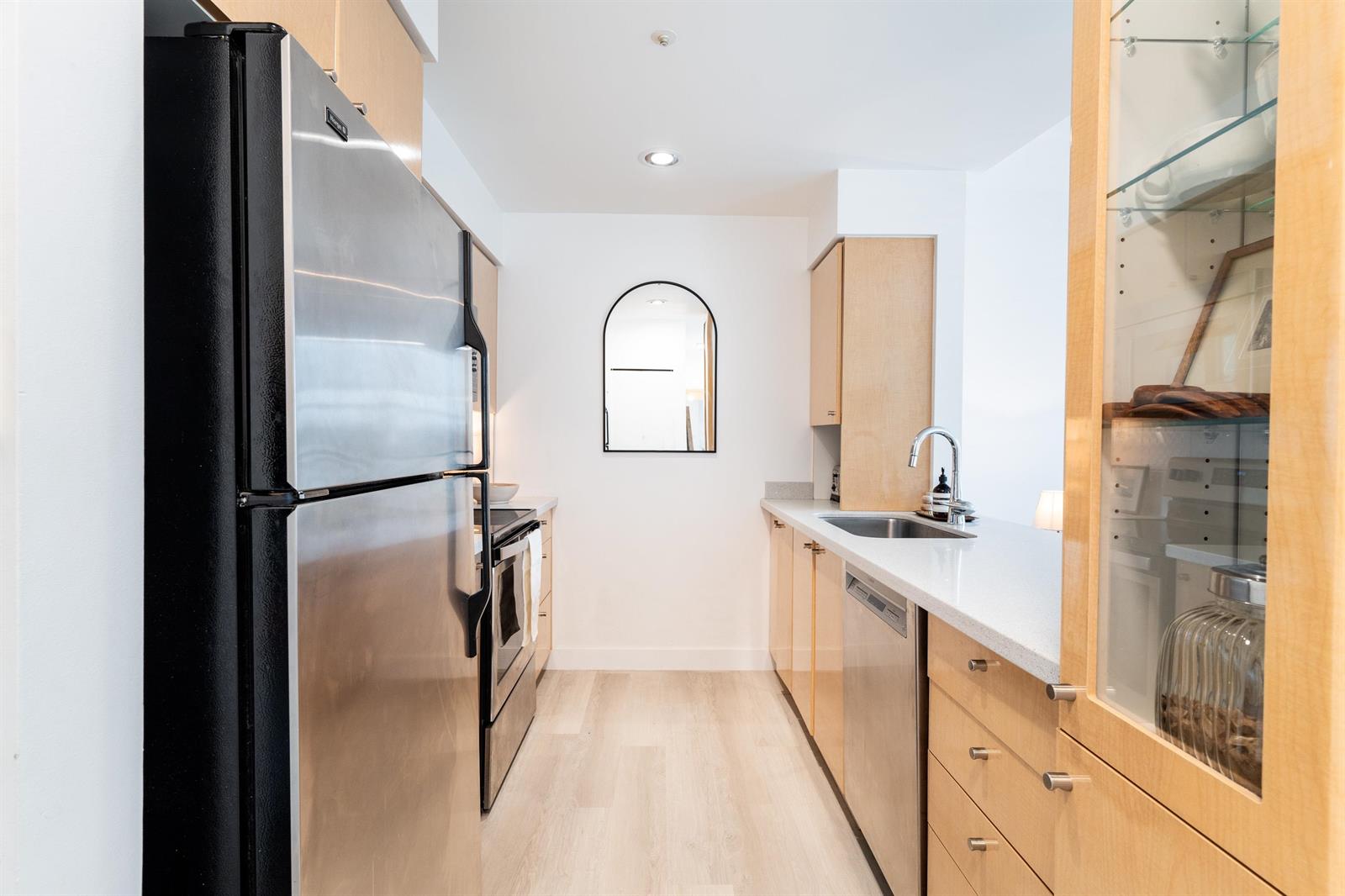 The kitchen from the entry end, refrigerator on the left and the counter running down to the arched mirror.