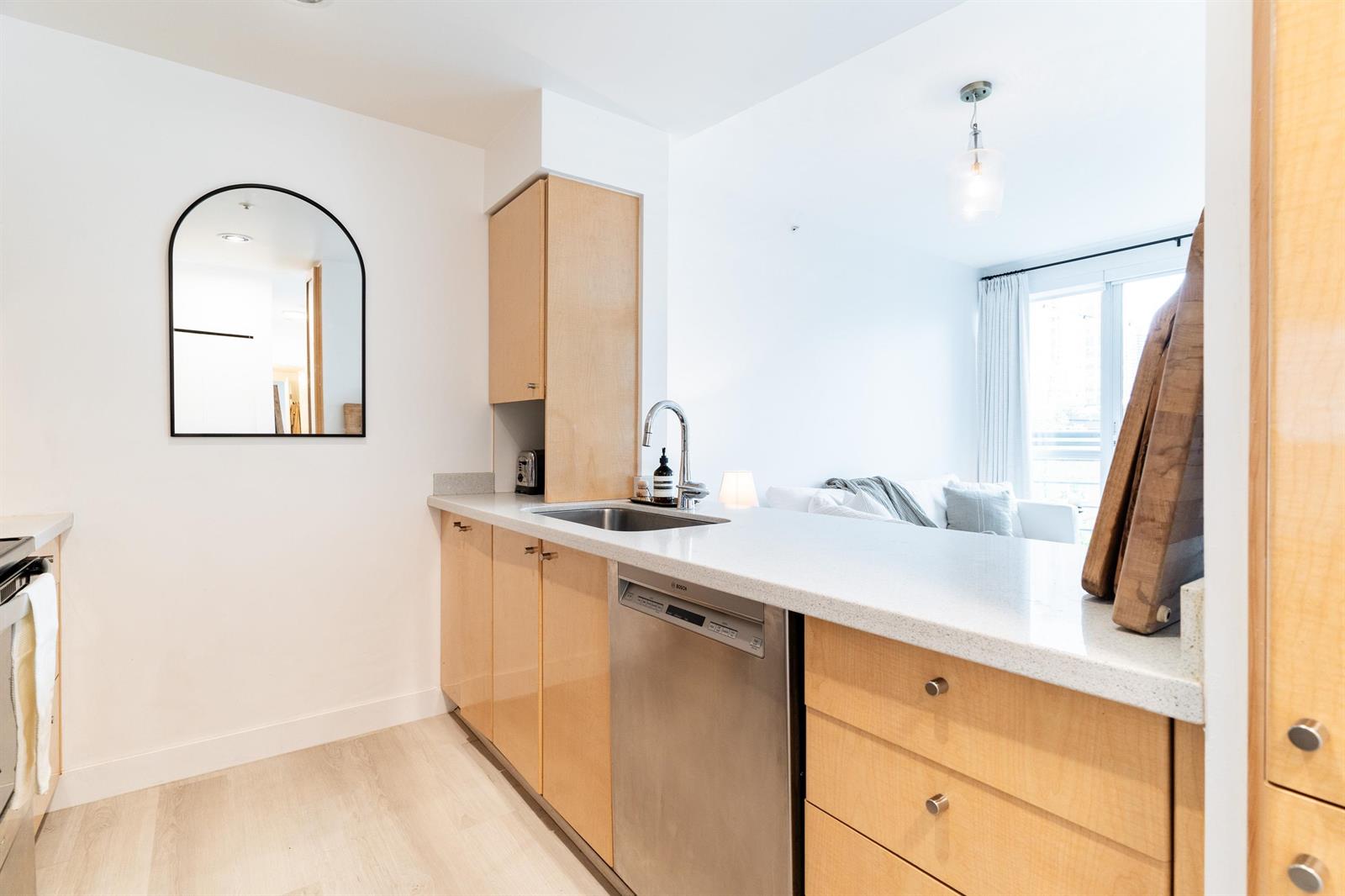 The kitchen from the far end, arched mirror above the sink, dishwasher set into the run of cabinets.