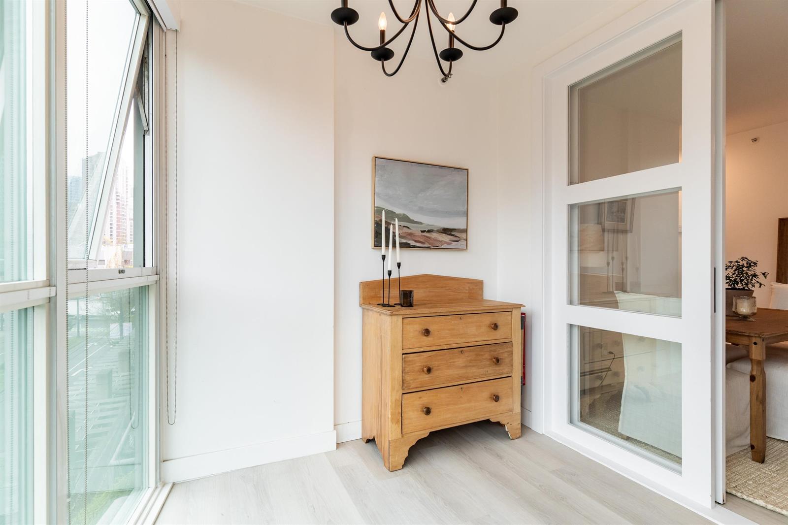 A corner of the second bedroom, a chest of drawers beneath the window with the chandelier above.