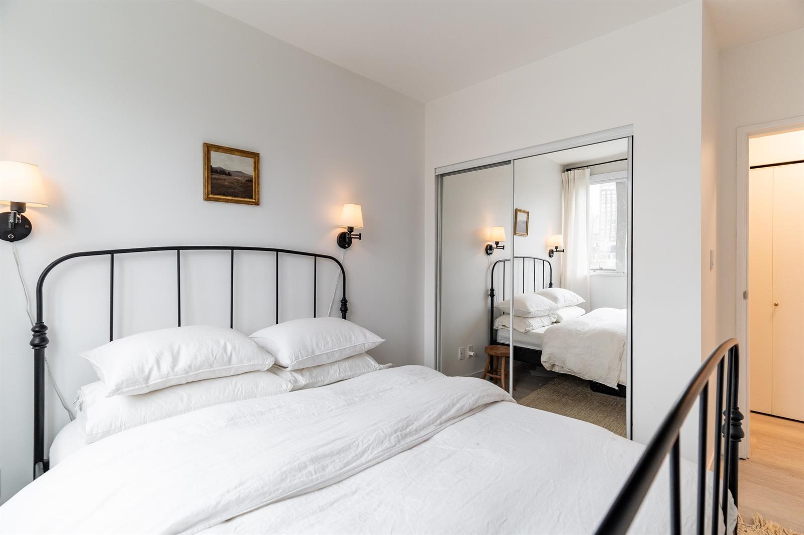 The main bedroom from the foot of the bed, a framed print and the mirror on the wall.