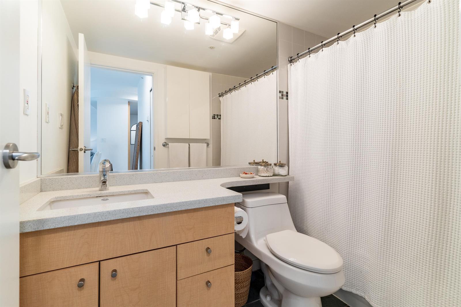 The bathroom, a wide mirror above the vanity and the tub behind a curtain.