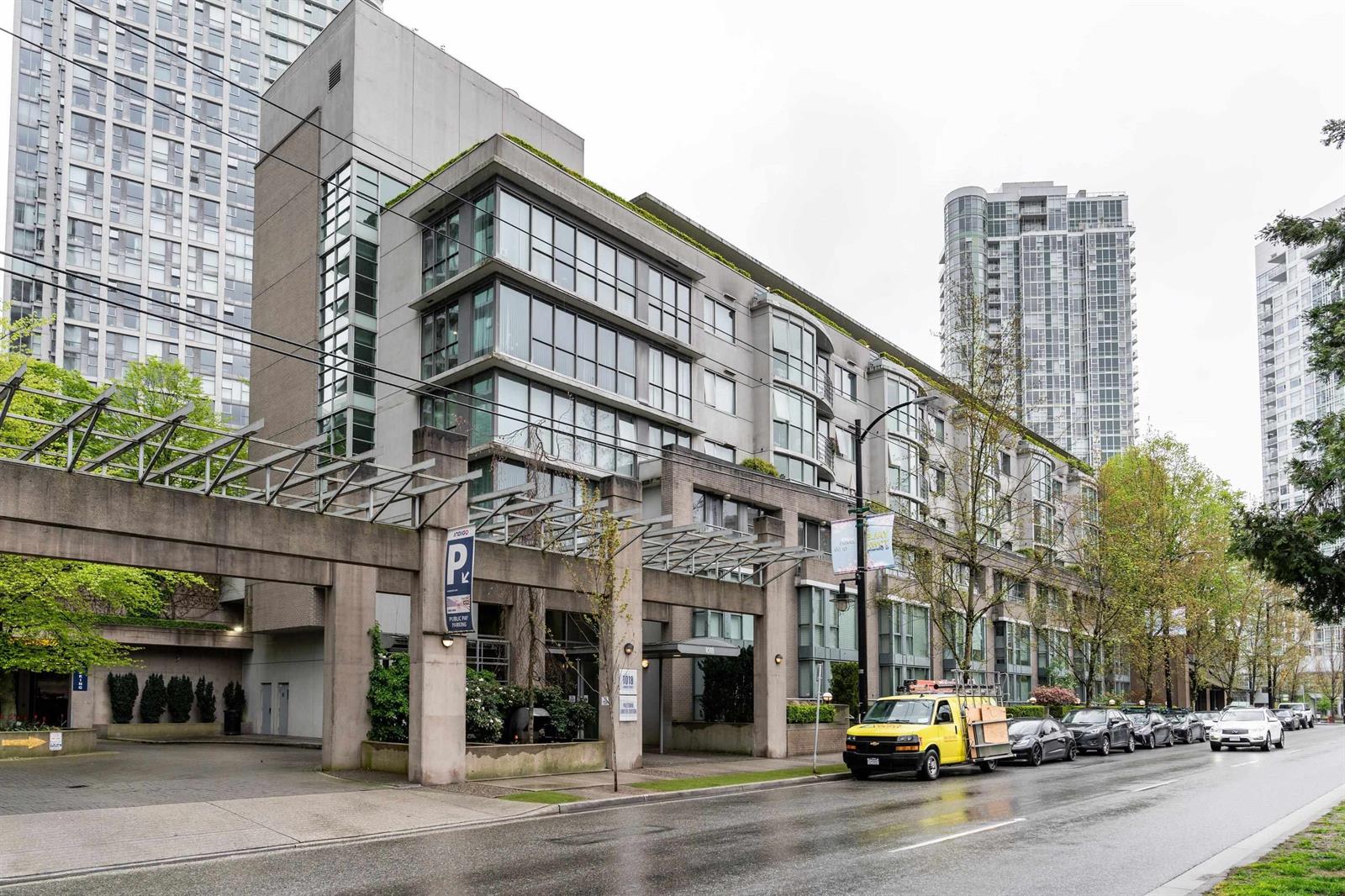 The complex from up the block, a low brick and glass building running along Cambie Street beneath the towers behind it.