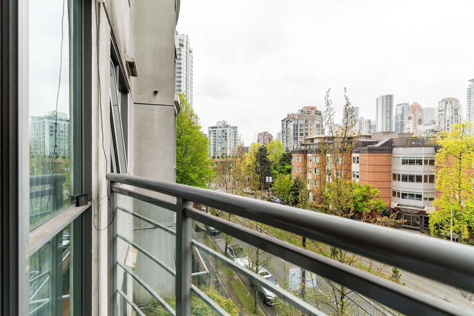 Along the balcony rail, the city towers rising past the trees.