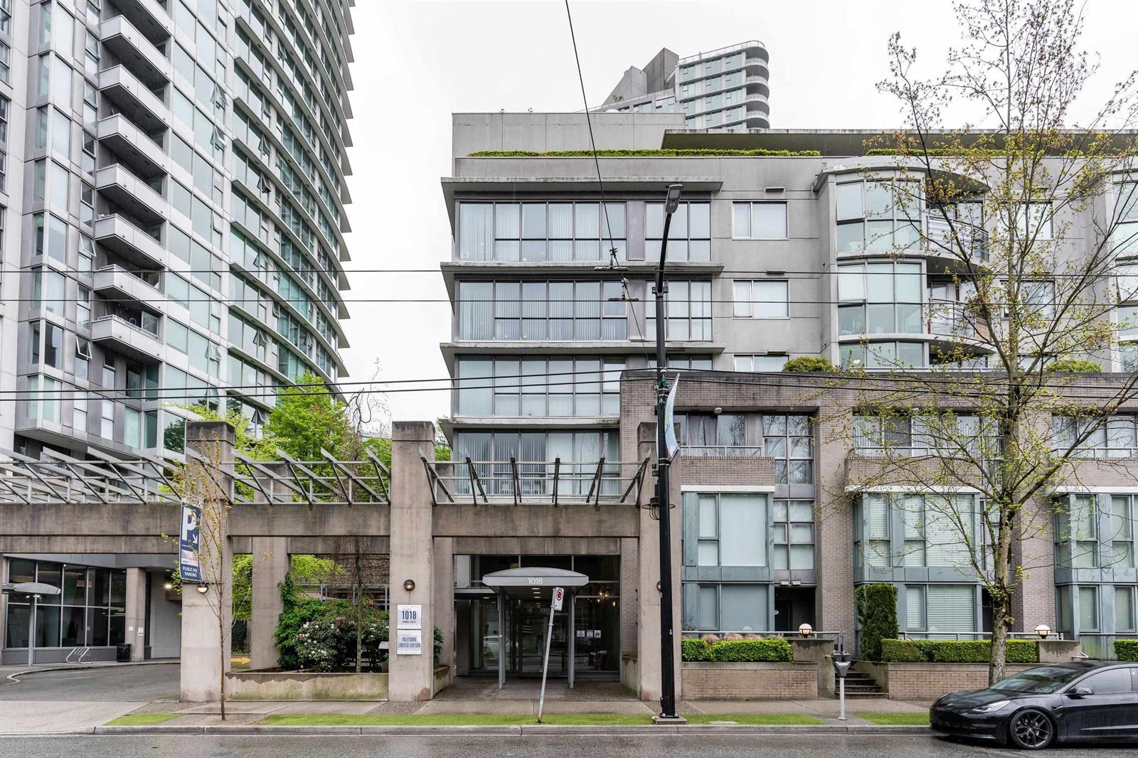 The building from across the street, the glass canopy over the entrance with a tower rising behind.