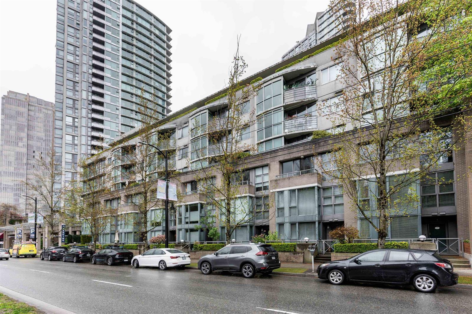 The block from the other direction, the low building and its balconies with cars along the curb.