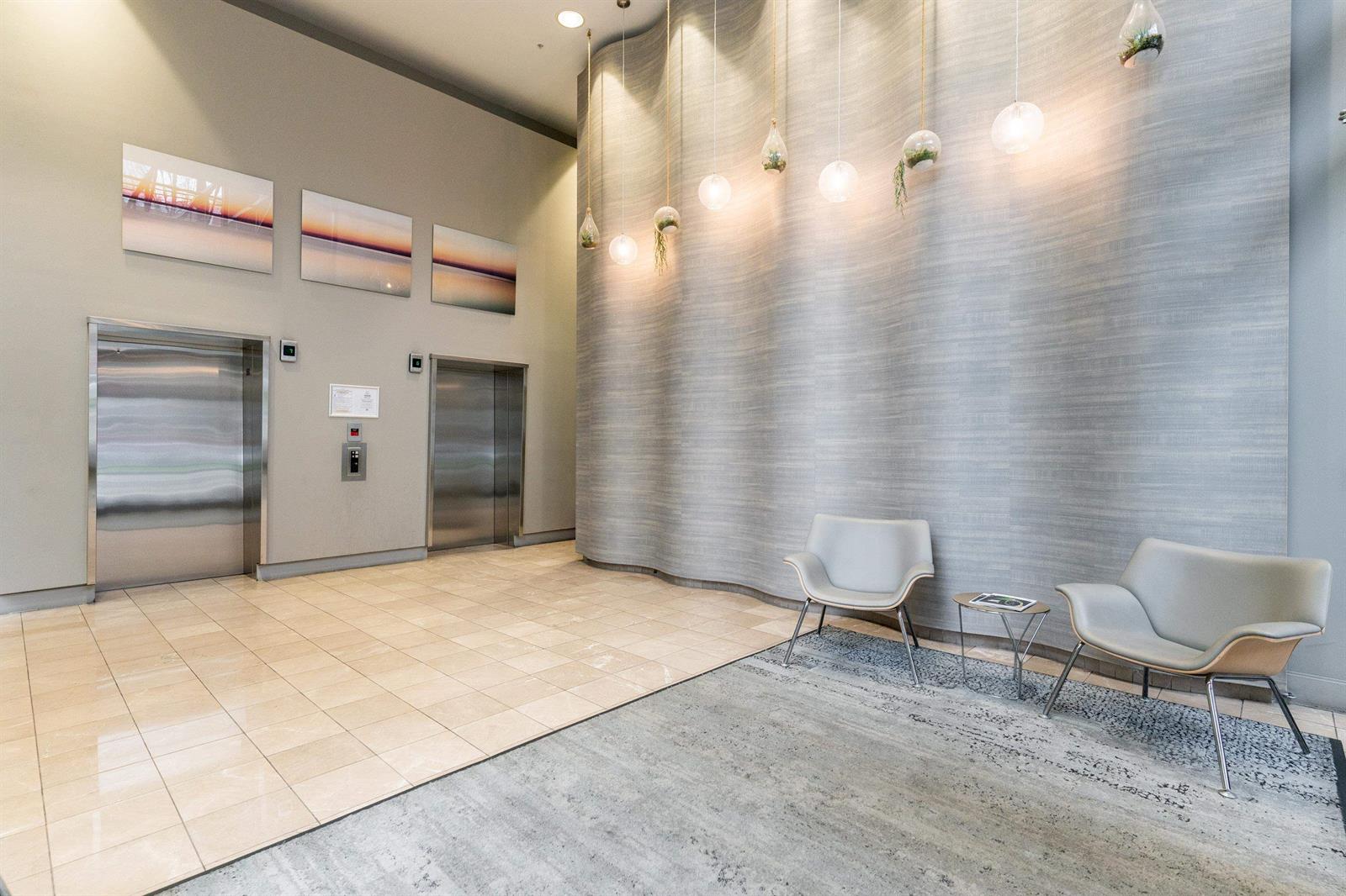 The lobby corridor, tiled floor and lit ceiling, with chairs at the far end.