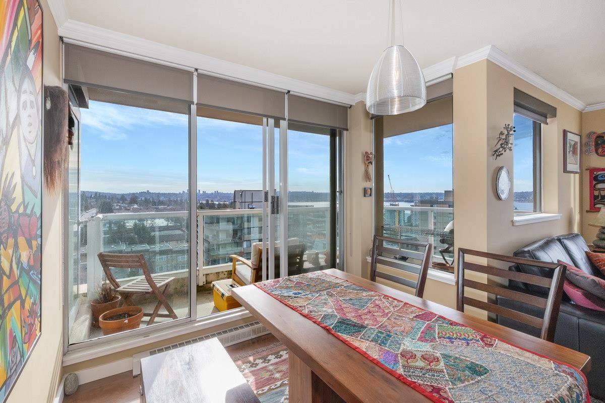 The dining end of the living room, a long table set against the glass with the inlet behind it.