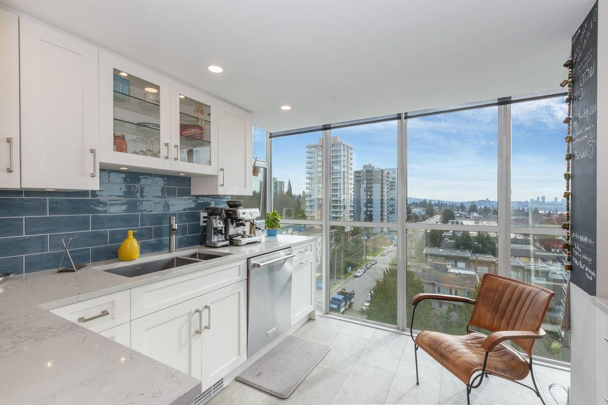 The kitchen, pale cabinets and a blue tiled splashback with the window wall running past it.