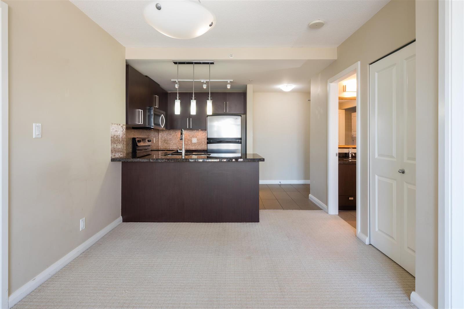 The kitchen seen across the floor, dark cabinets under track lighting with the hall doors beside it.