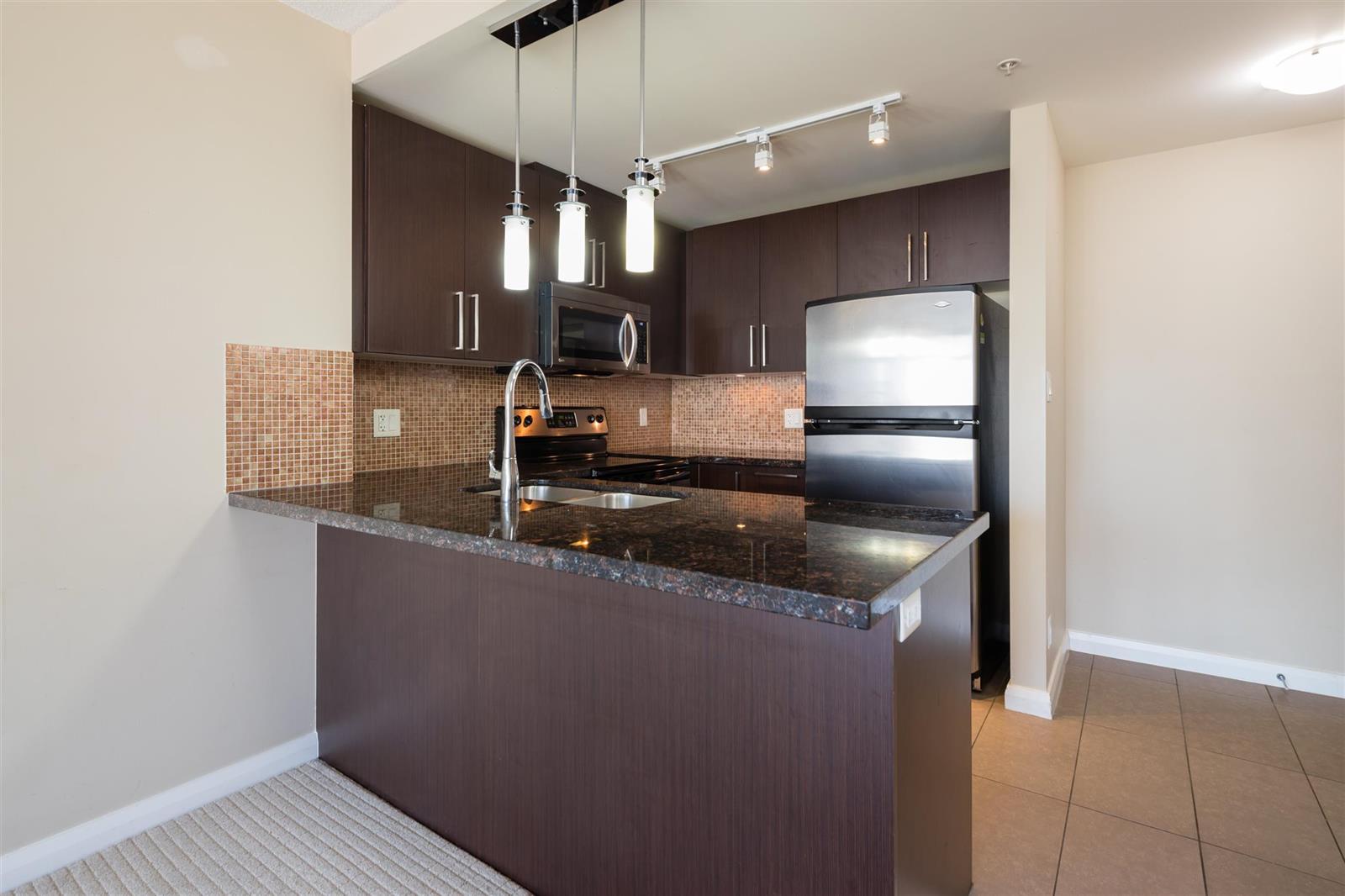 The kitchen, granite counters and a stainless fridge with pendants over the peninsula.