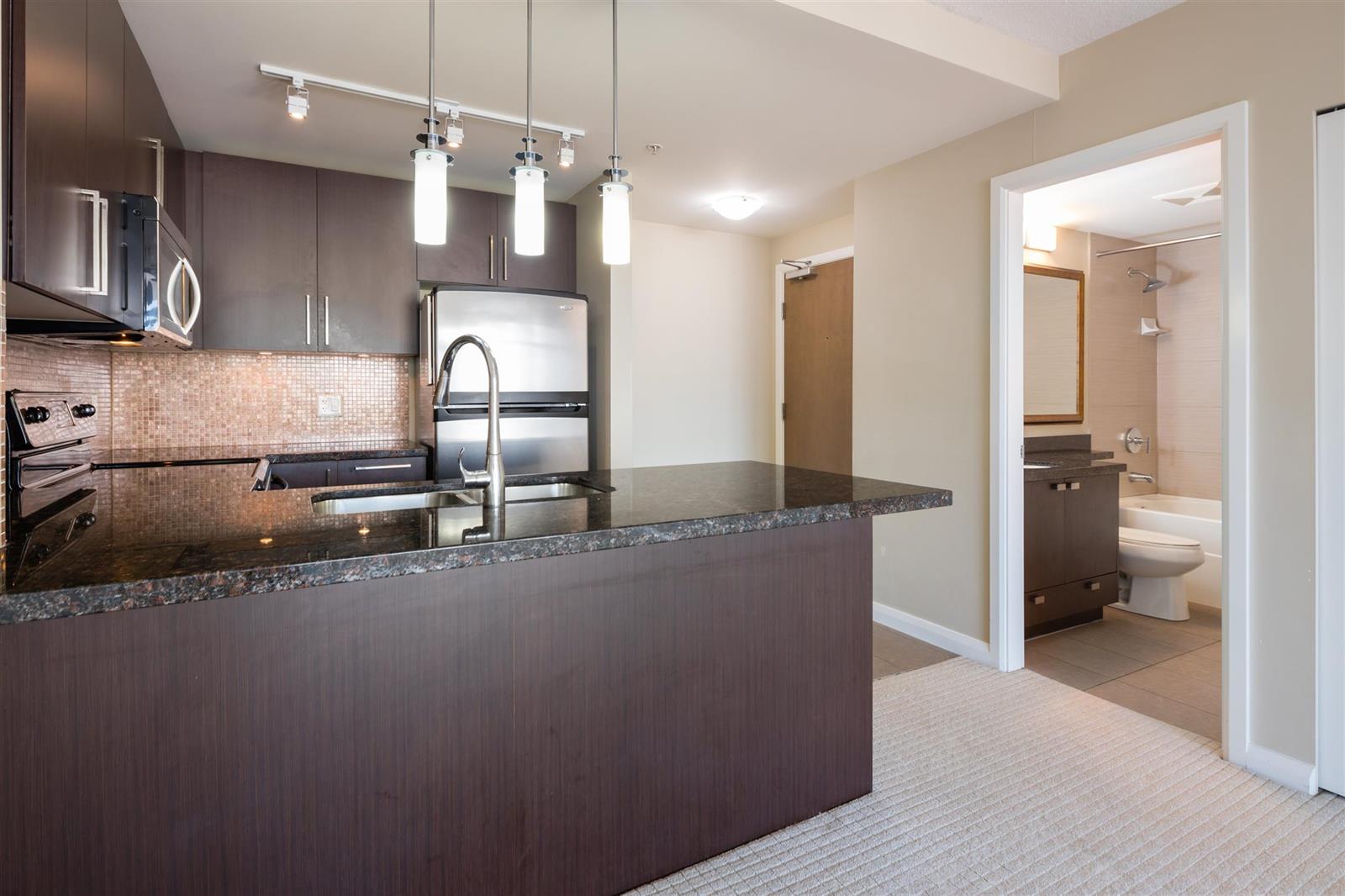 The kitchen from the other end, the range and cabinets in a row and a bathroom door standing open.