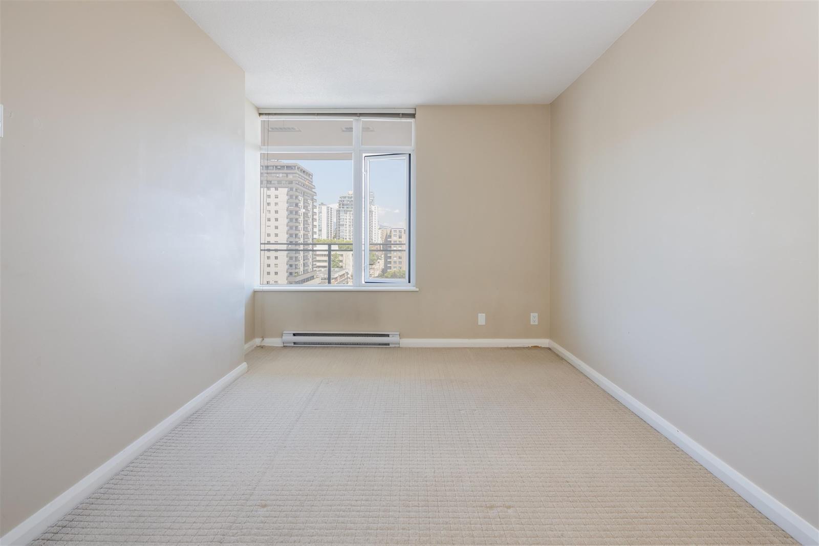 A bedroom corner, the window carrying the buildings and the sky.