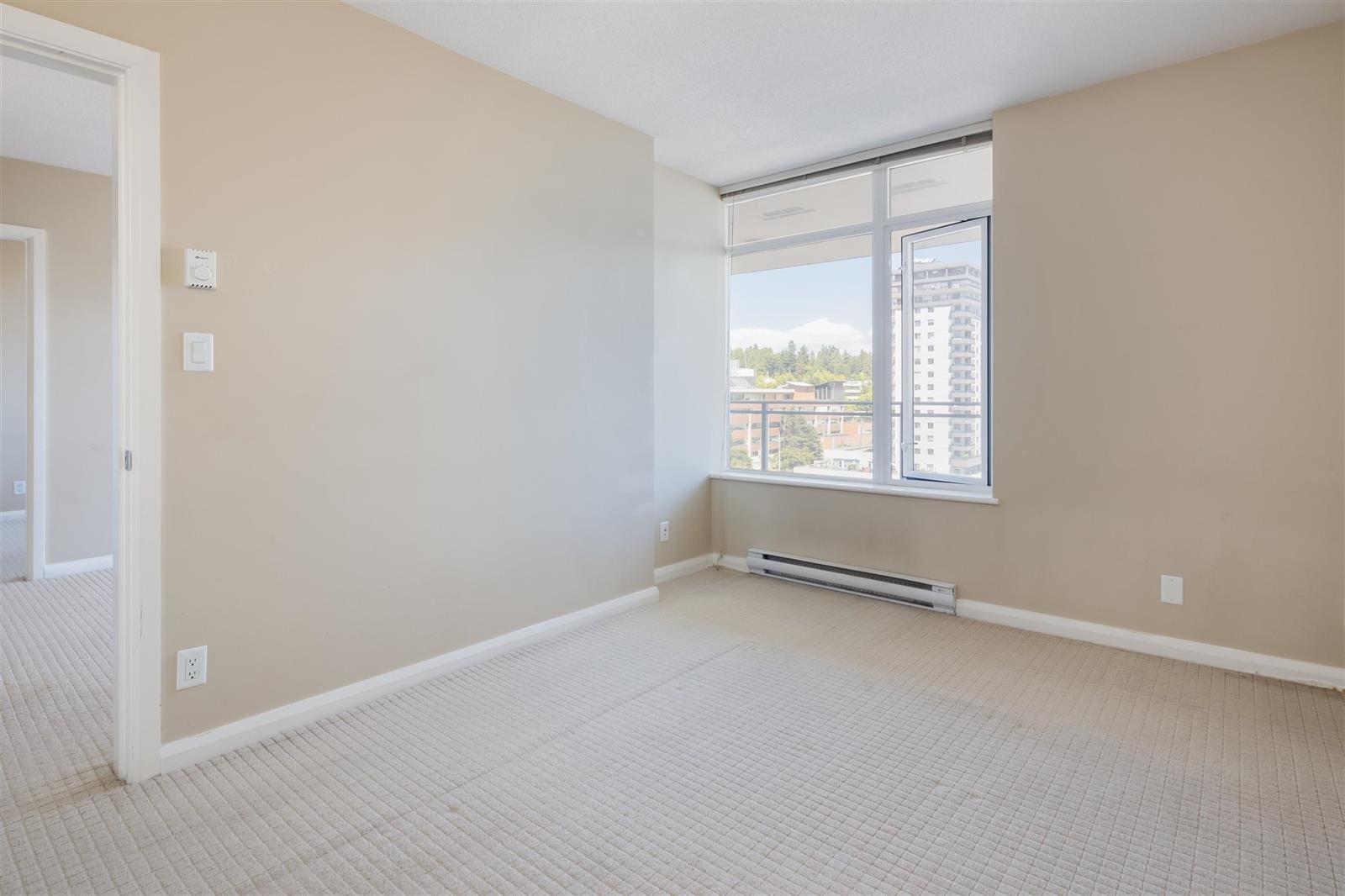 A bedroom from the doorway, the window at the far end with the city in it.