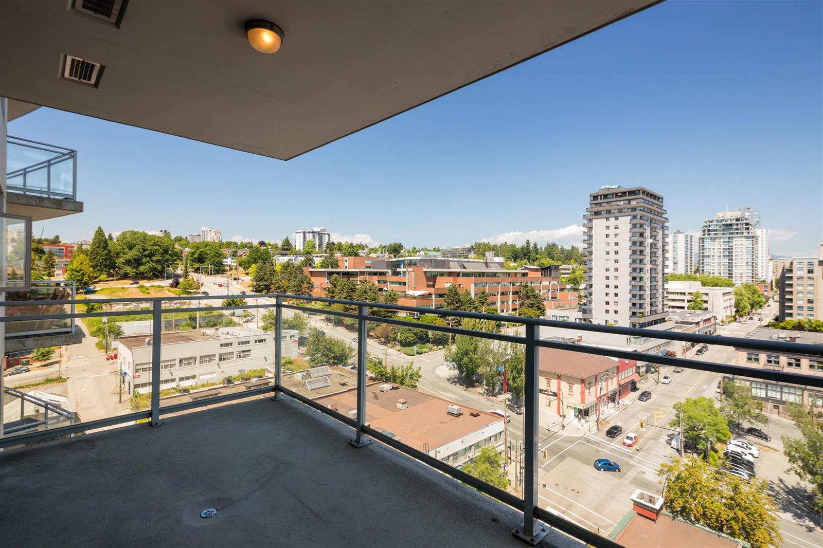 The patio, a glass rail along its edge with the towers and treetops past it.
