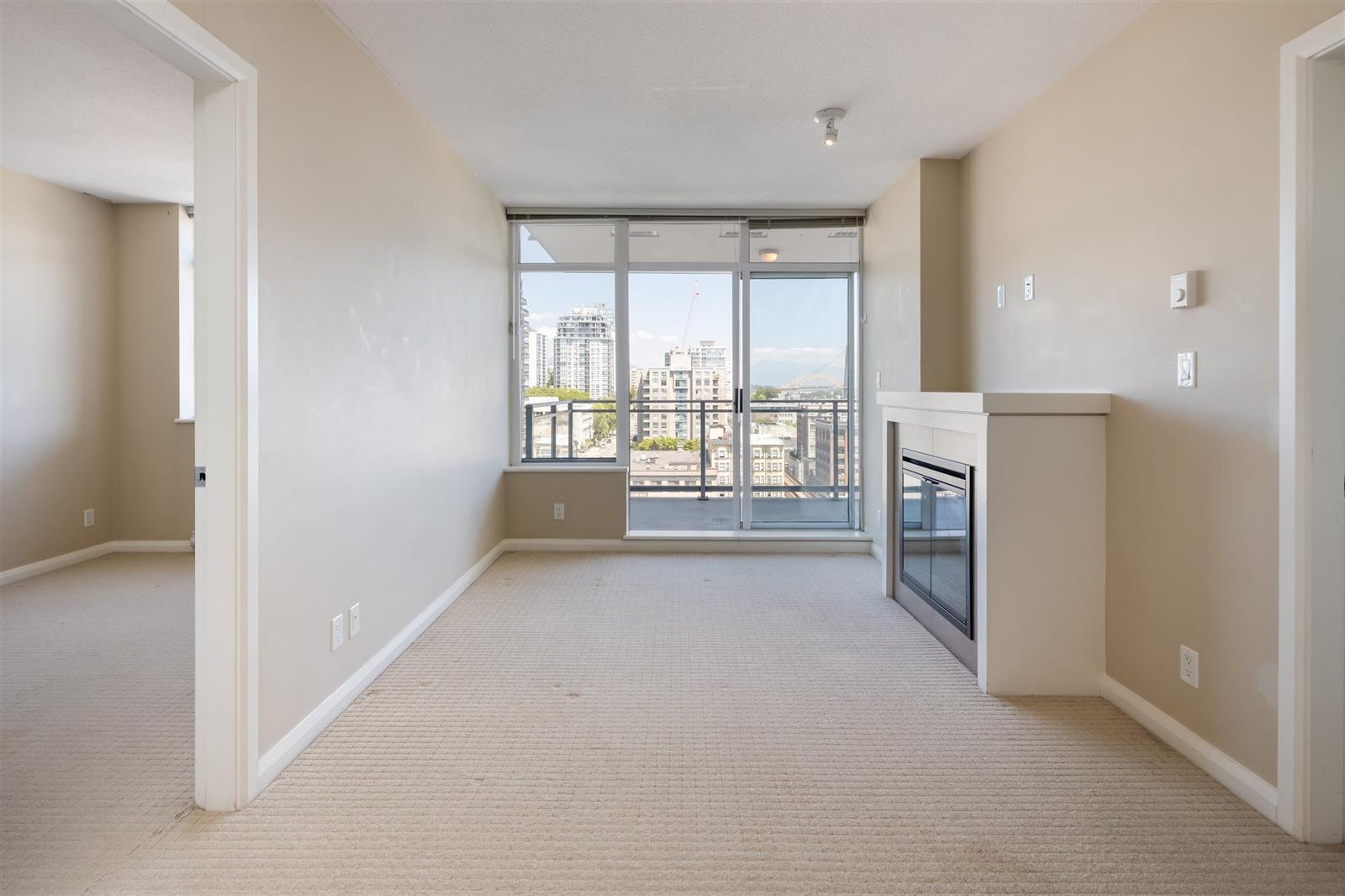The empty living and dining rooms, windows across the far wall and the patio door in the corner.