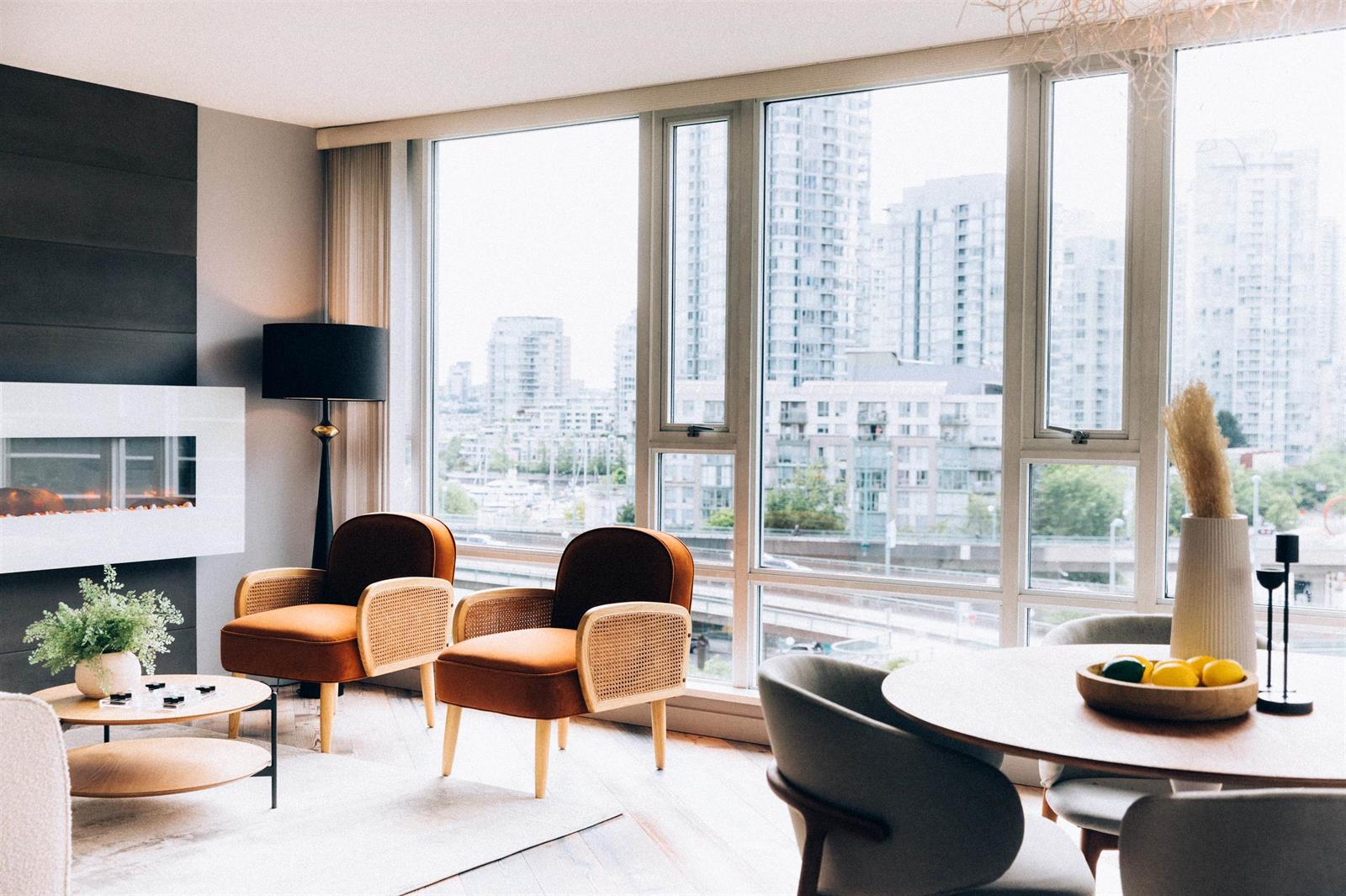 The living room along the window wall, the fireplace and a floor lamp beside chairs drawn up to the glass, with the city outside.