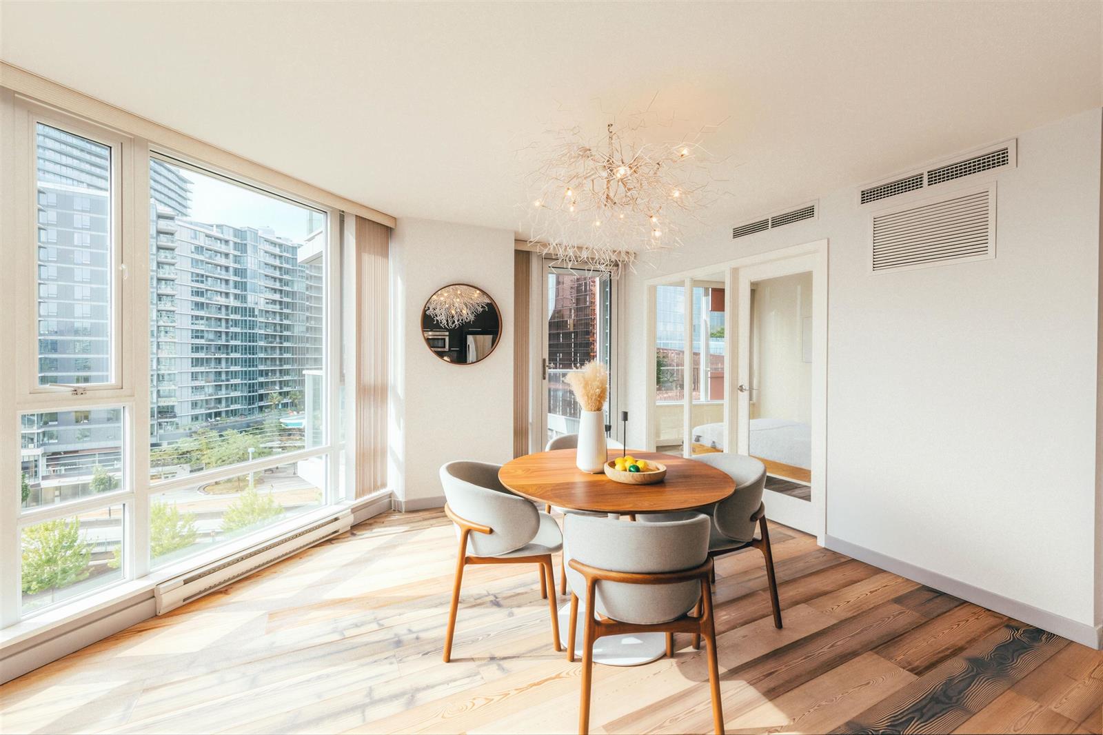 The dining area from the kitchen, the round table and chandelier against the windows.