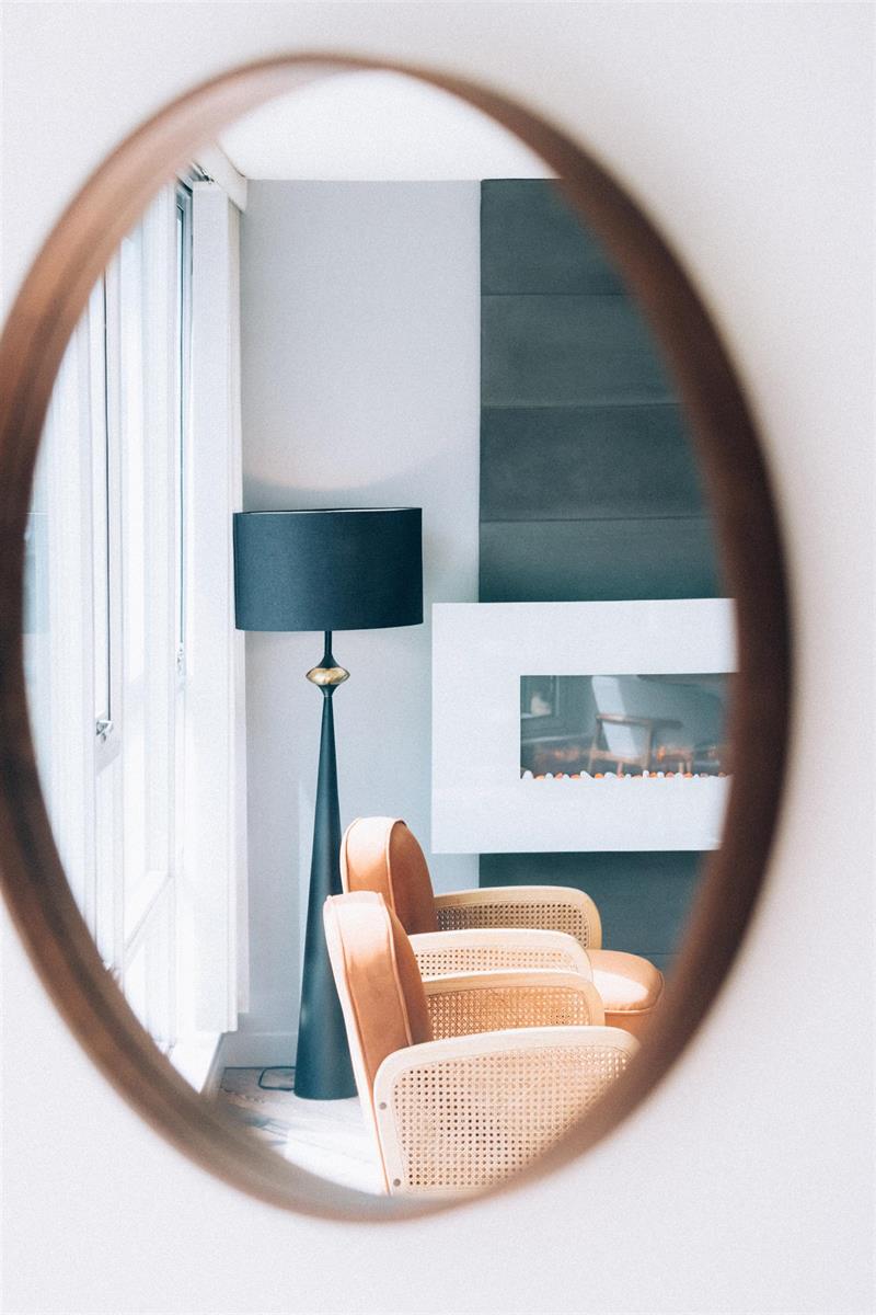 A round mirror on the wall, carrying the lamp, the chairs and the fireplace back into the room.
