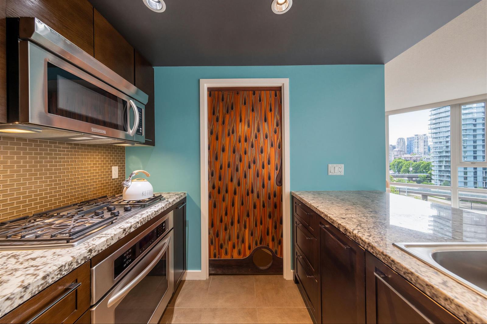 The kitchen, the gas range under wood cabinets with the pantry door beyond.