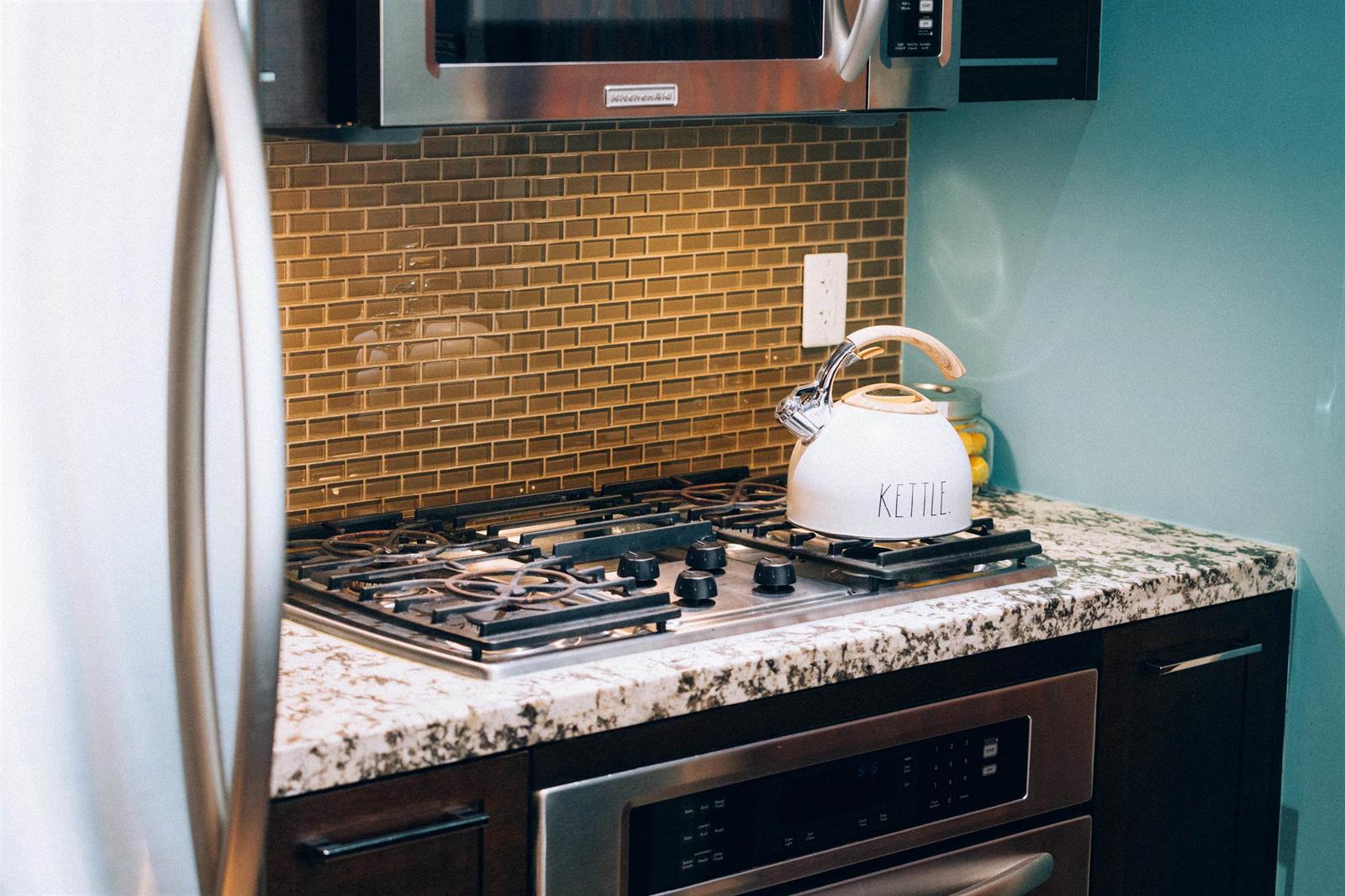 The gas cooktop and the wall oven, a kettle on the burner and tiled backsplash above.