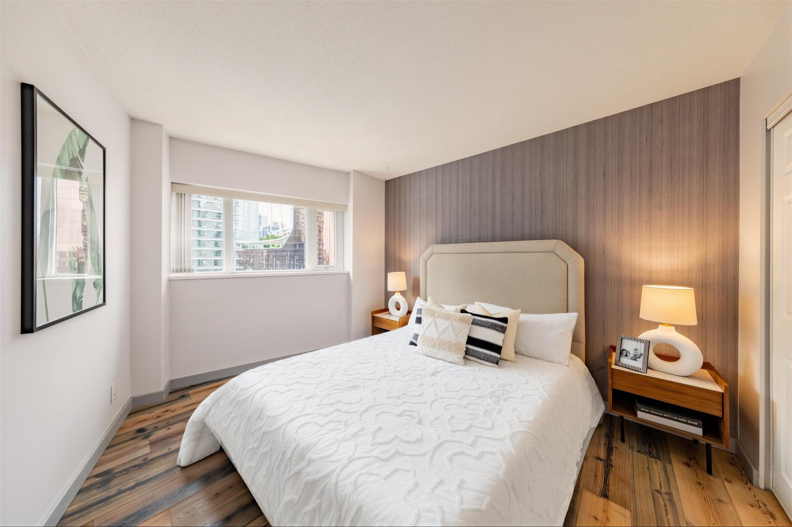 The same bedroom from the doorway, artwork above the bed and the window beyond.
