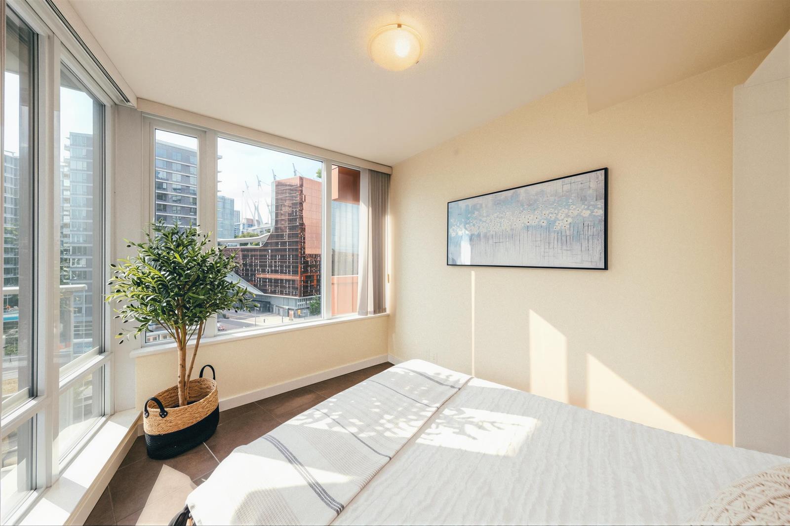 A bedroom with windows down one side, a plant in the corner and the bed under the glass.