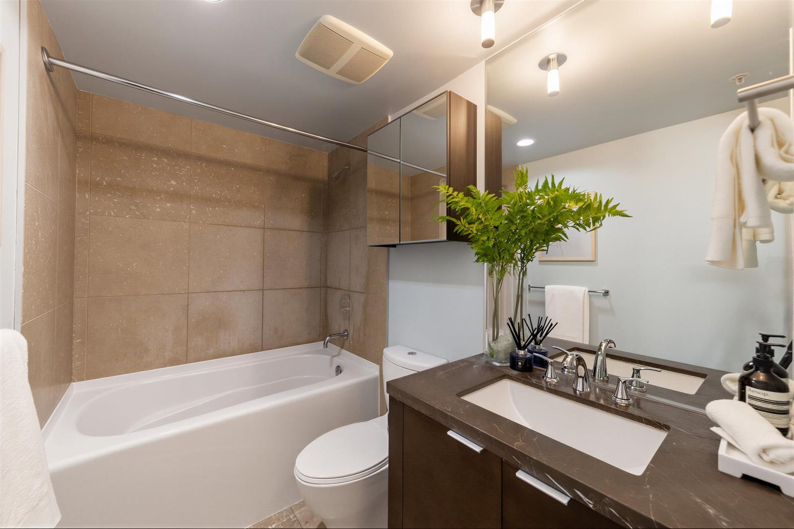 The bathroom, a tub under its tiled surround with the vanity and mirror beside it.