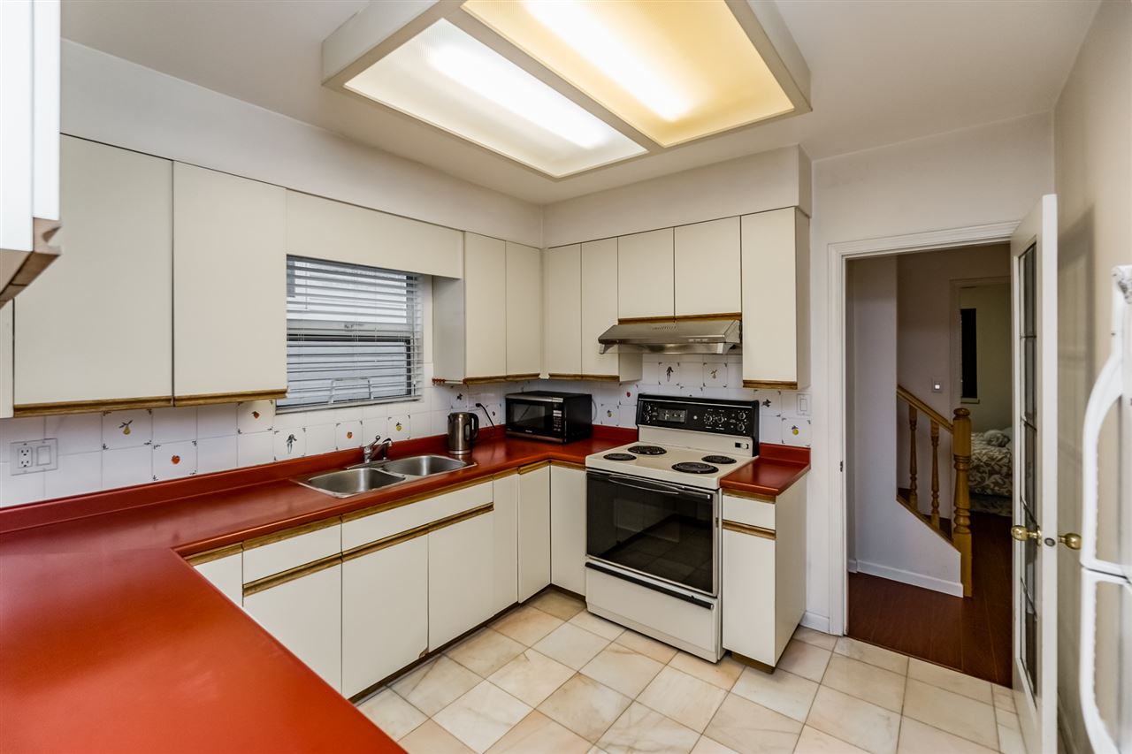The kitchen, white cabinets around a red counter with the range and the window over the sink.